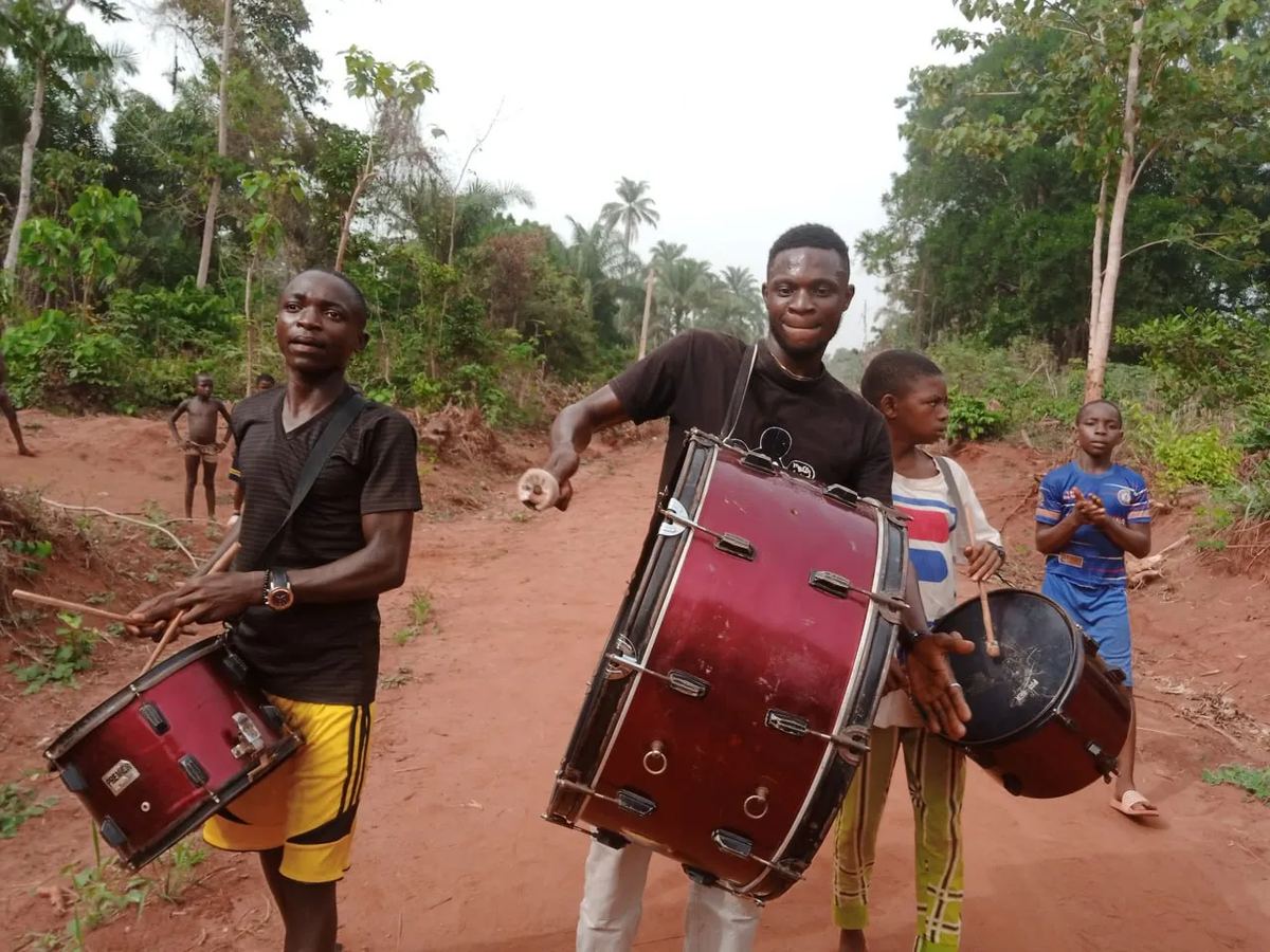 Young men drumming as they lead the team along a village road