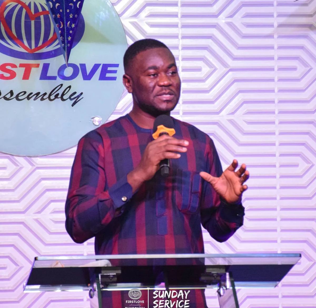 A preacher with a microphone at the lectern of First Love Assembly