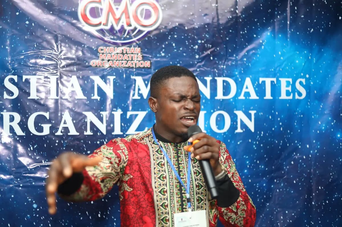 A minister preaching with a microphone in front of a Christian Mandates Organization banner