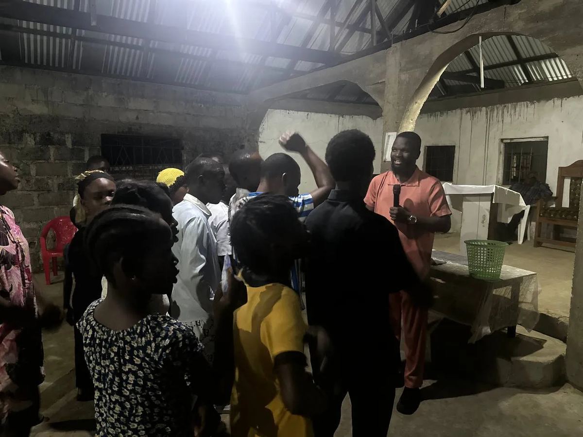 Young people standing at the front of a church as a man in orange leads them with a microphone