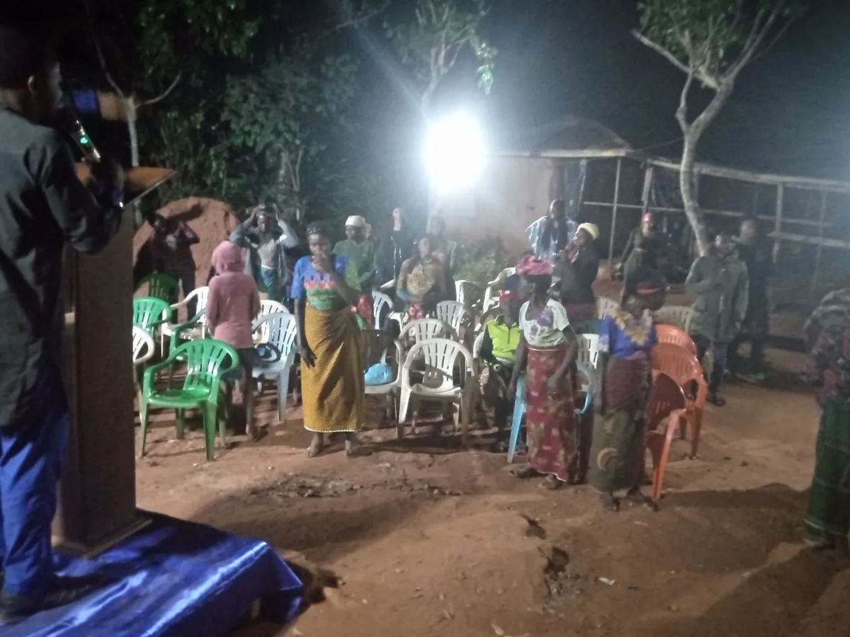 People standing among plastic chairs under a floodlight at the night outreach