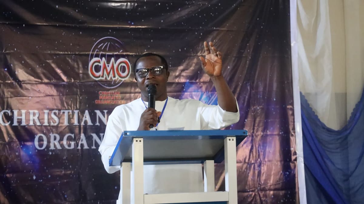 A speaker in white raising his hand as he preaches at the lectern in front of the CMO banner
