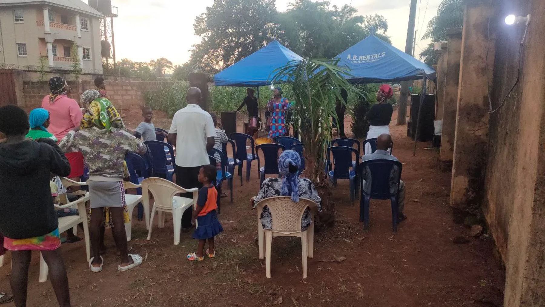 People gathering on chairs under blue canopies at dusk