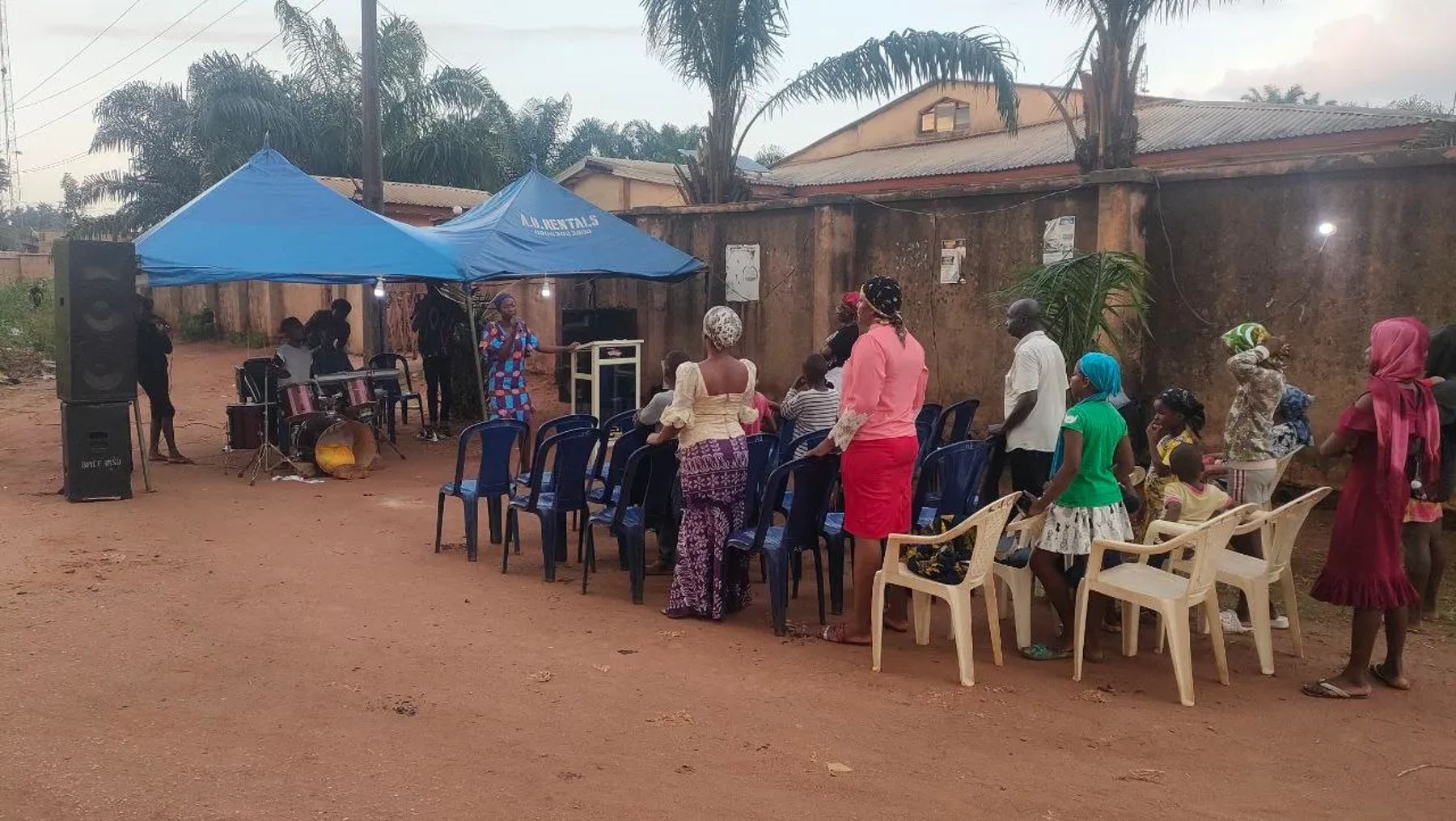 People standing among the chairs under blue canopies