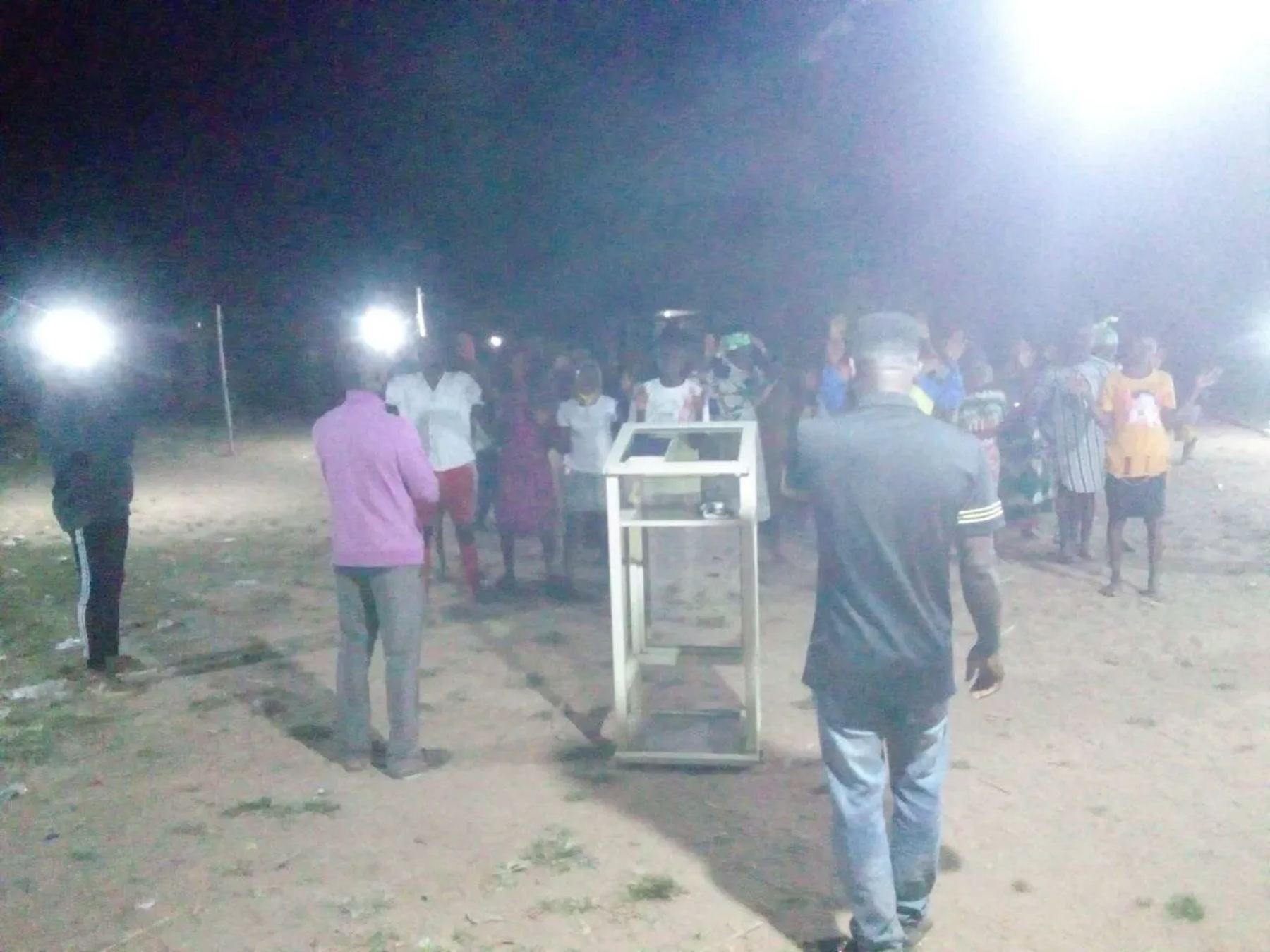 The team leading a night meeting under floodlights around a lectern