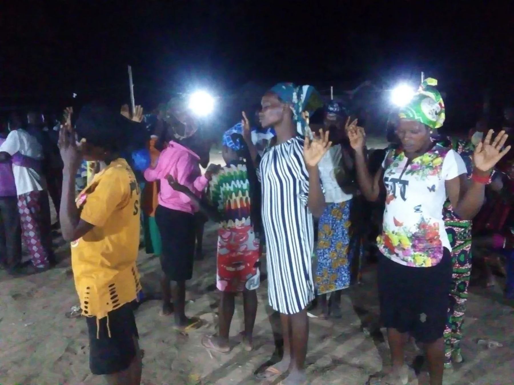 Women worshipping with raised hands under floodlights