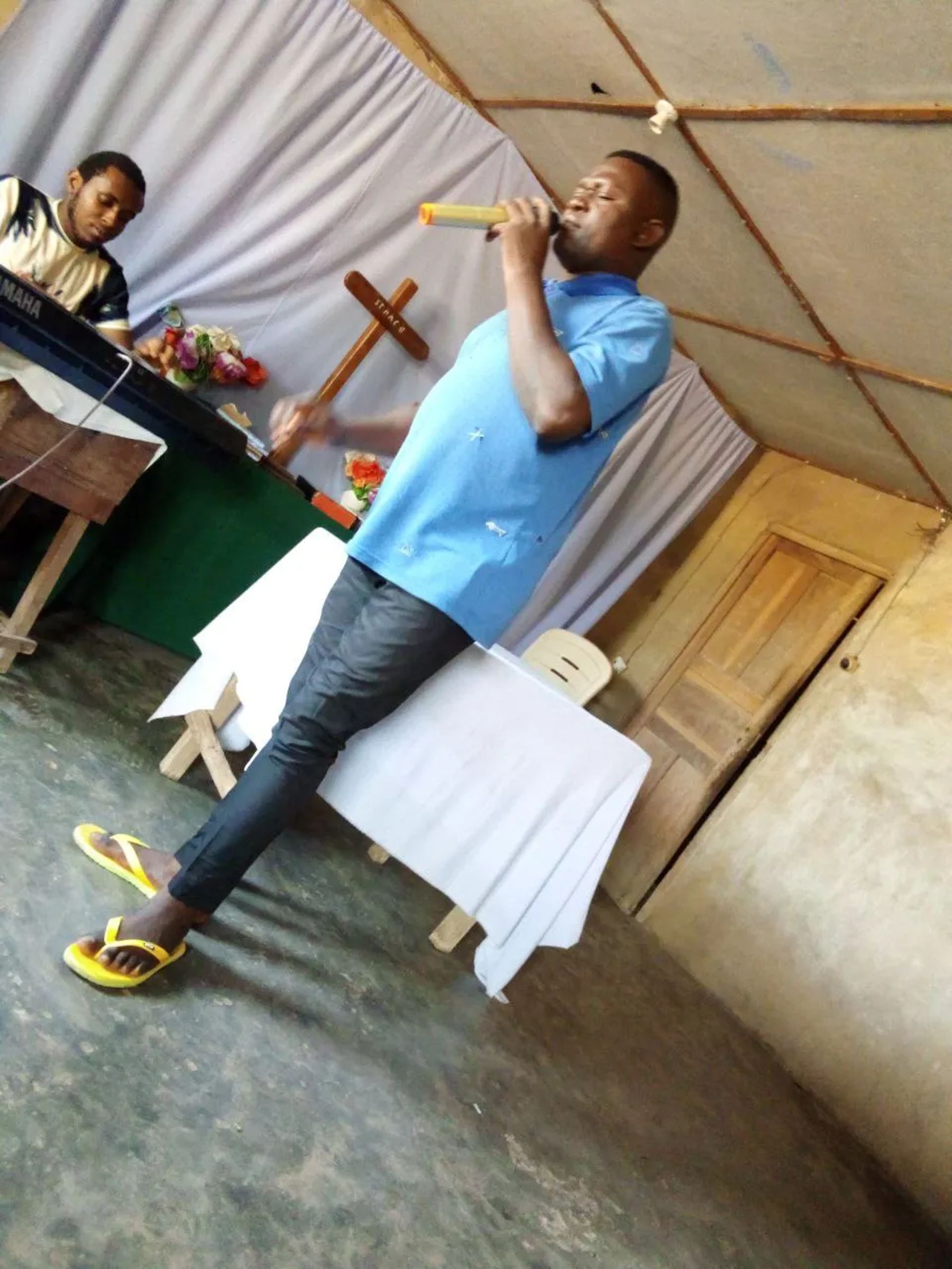 A preacher with a microphone inside a church, a cross on the table