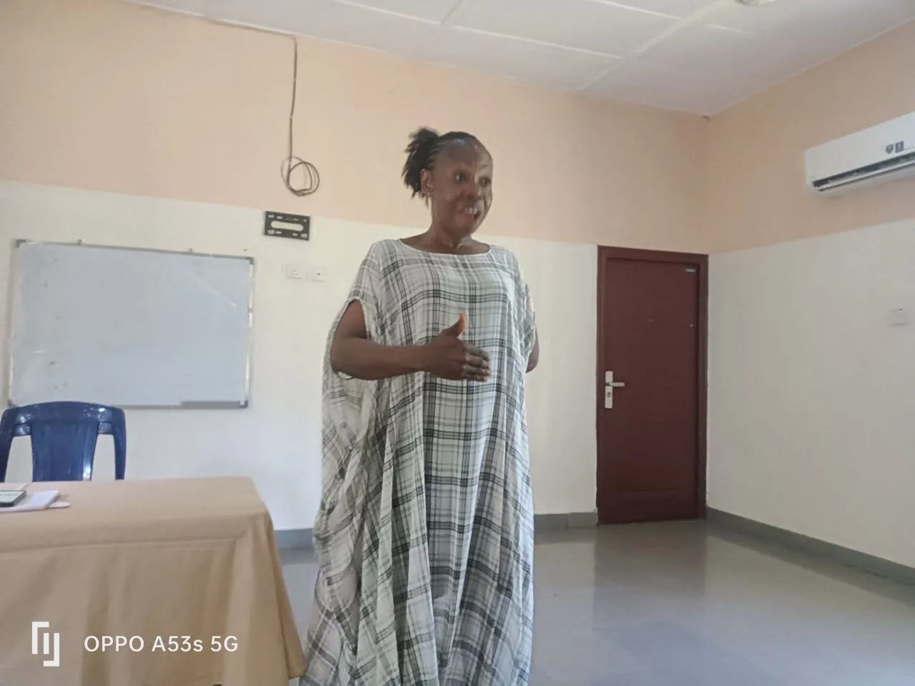 A speaker in a long checked dress addressing the hall, with a whiteboard behind her