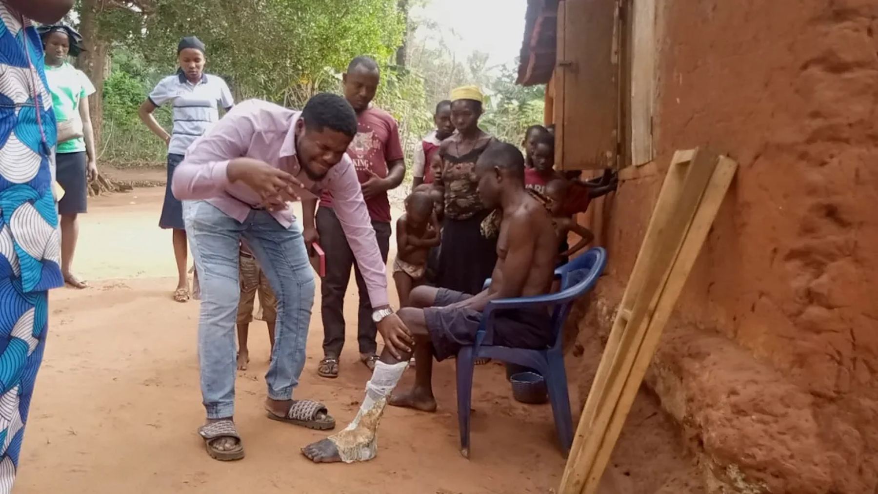 A team member praying for a man with an injured leg outside his house