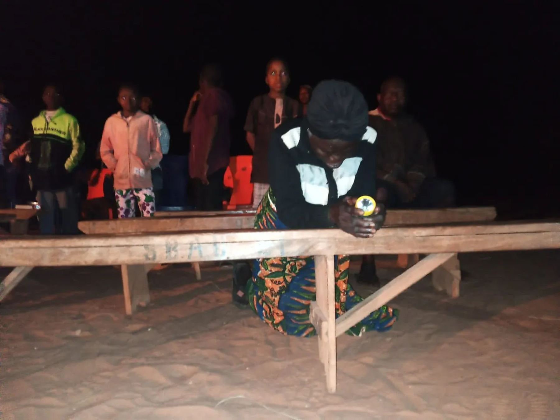 A woman kneeling in prayer at a wooden bench at night