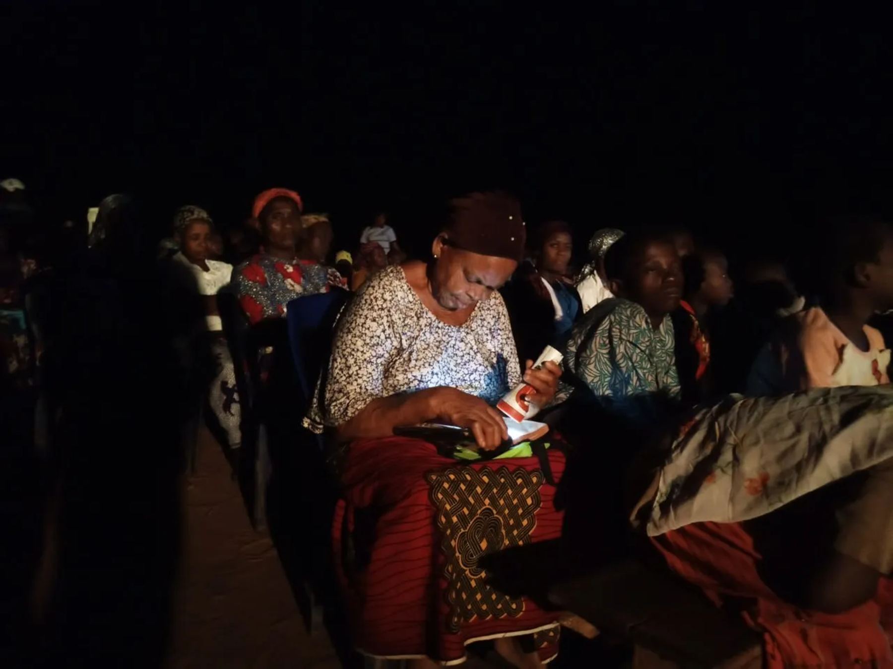 A woman reading by phone light at the night meeting