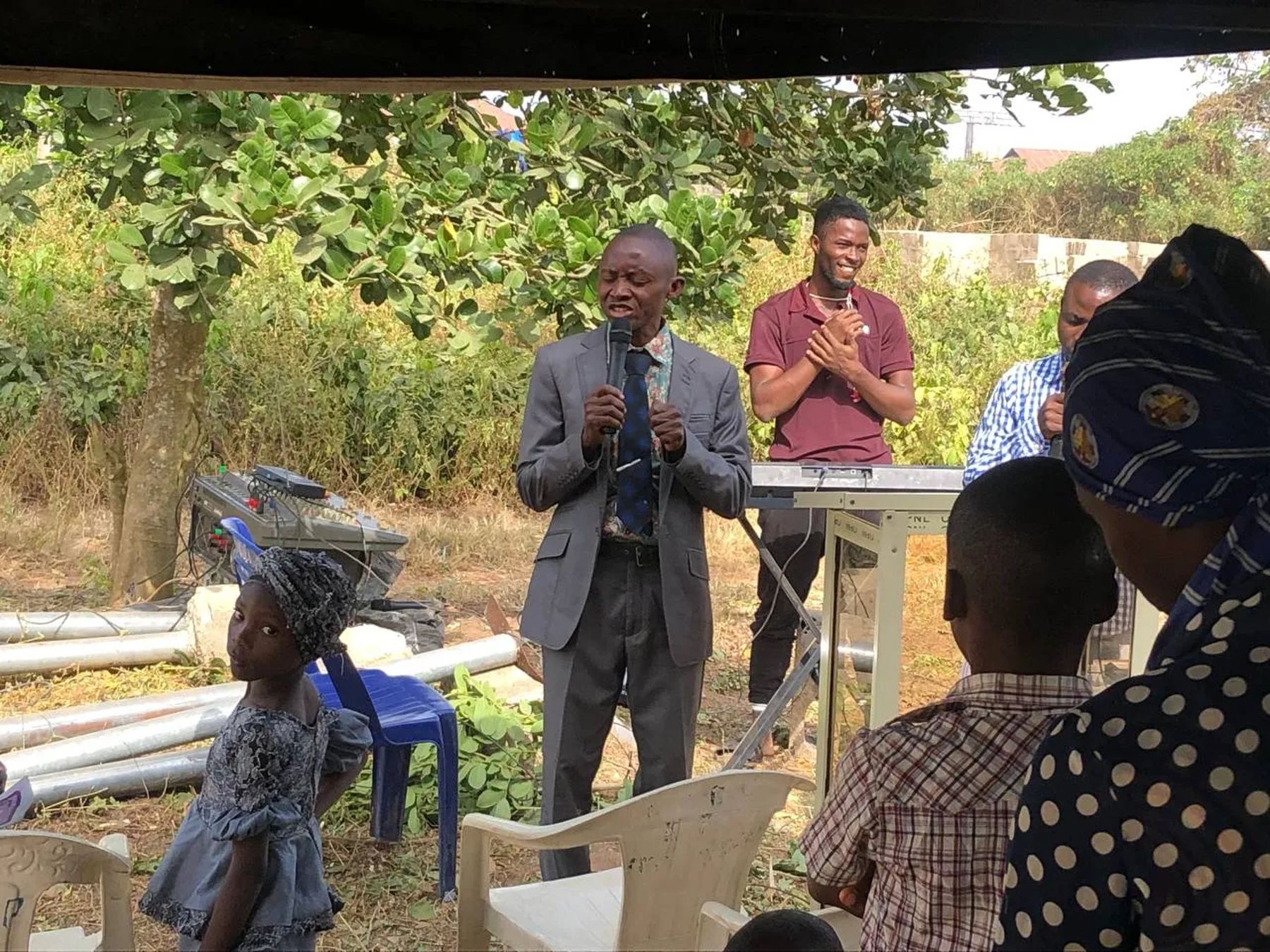 A preacher with a microphone speaking to a small group seated outdoors