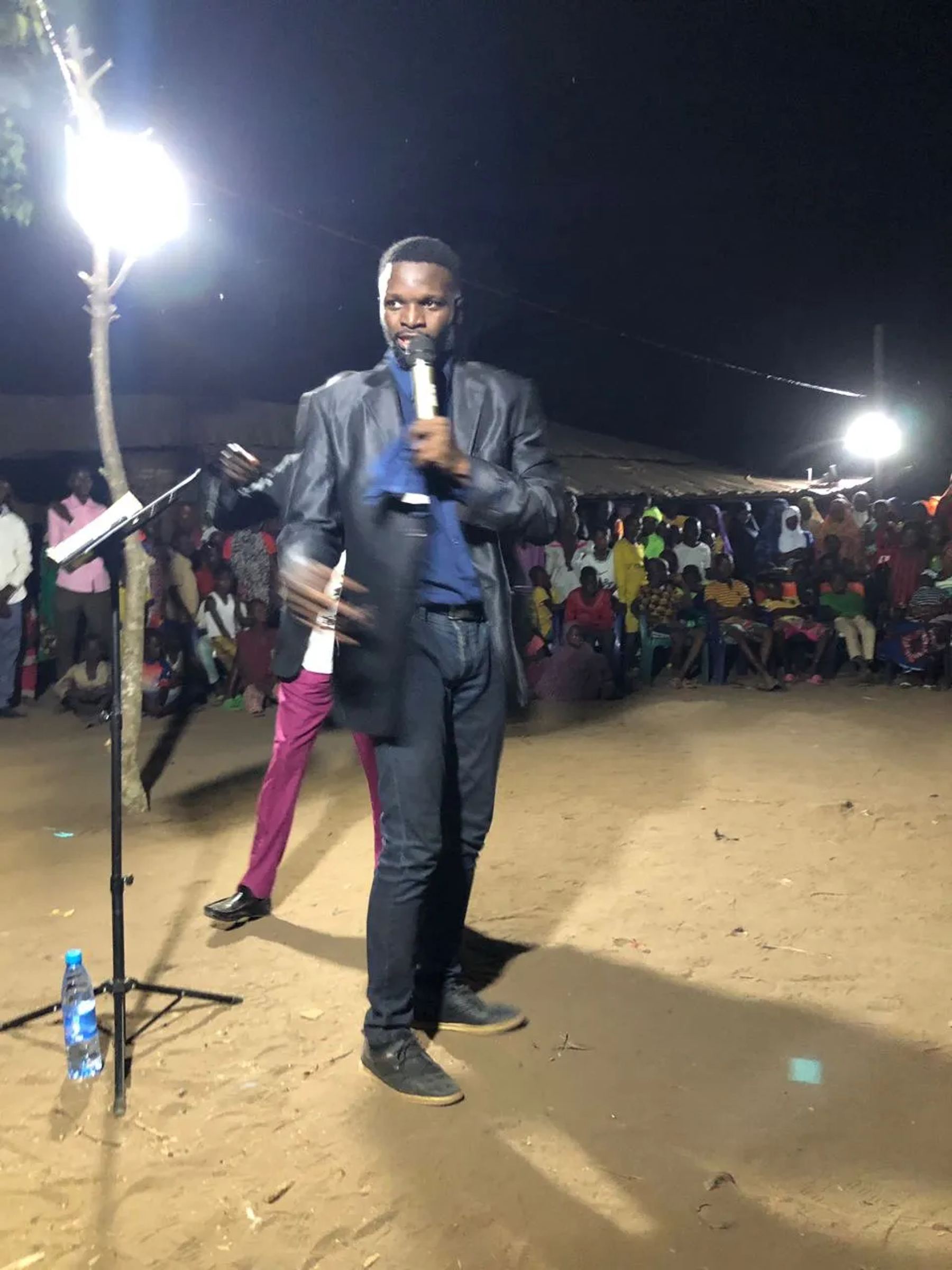 A preacher with a microphone at the night meeting under floodlights