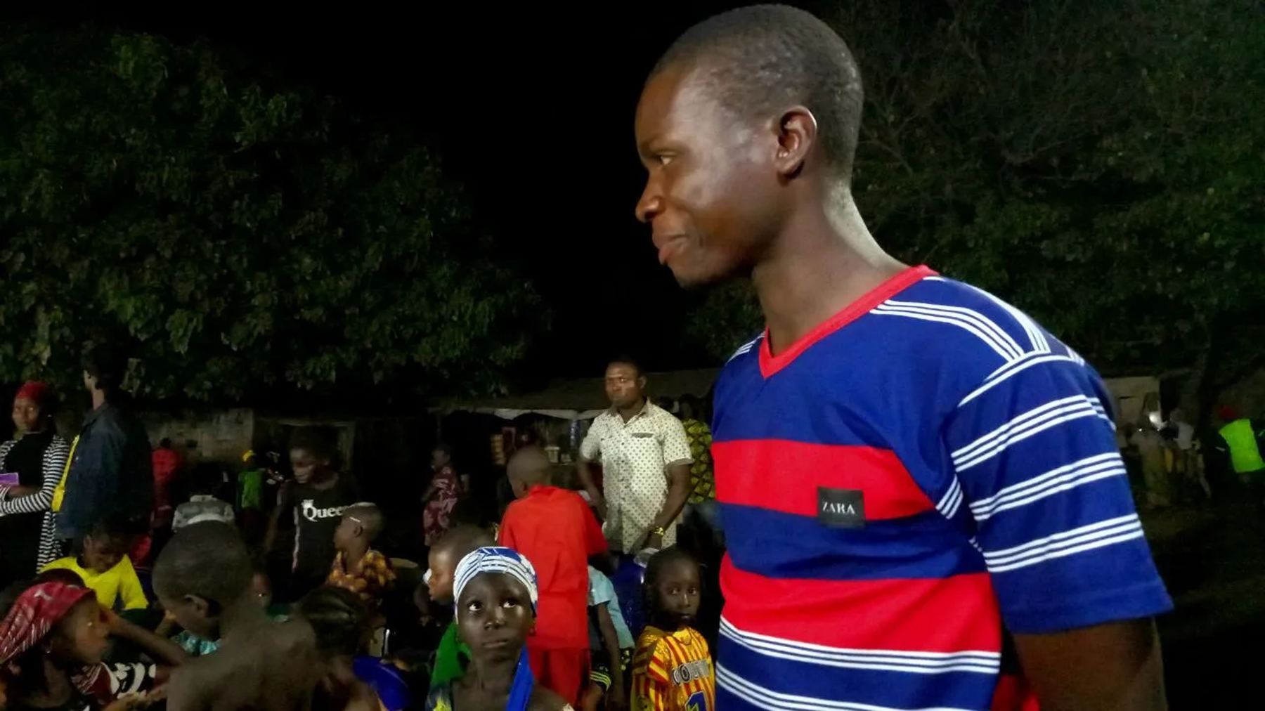 A team member at the night meeting, with children seated behind