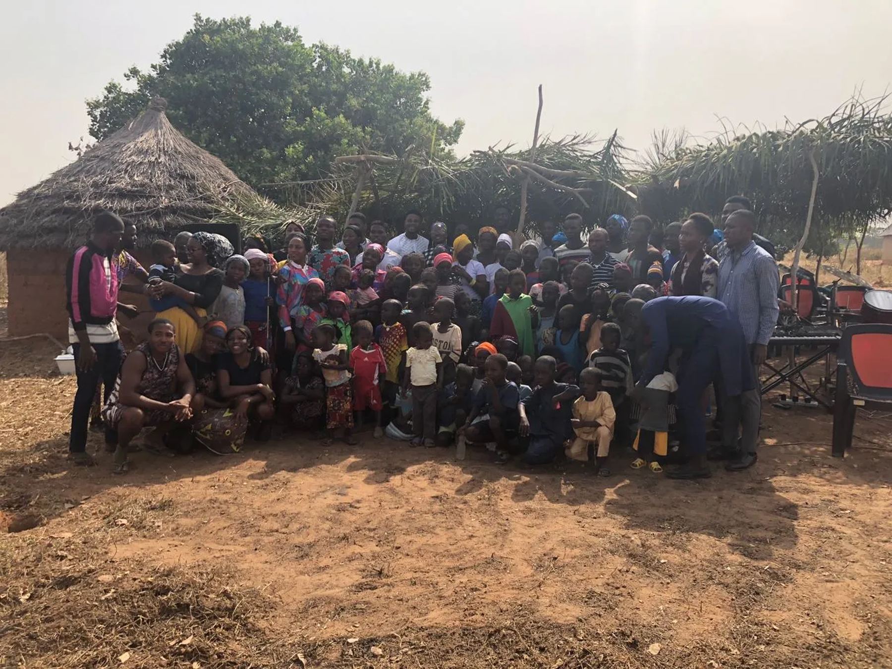 The team with a large crowd of villagers in front of thatched huts