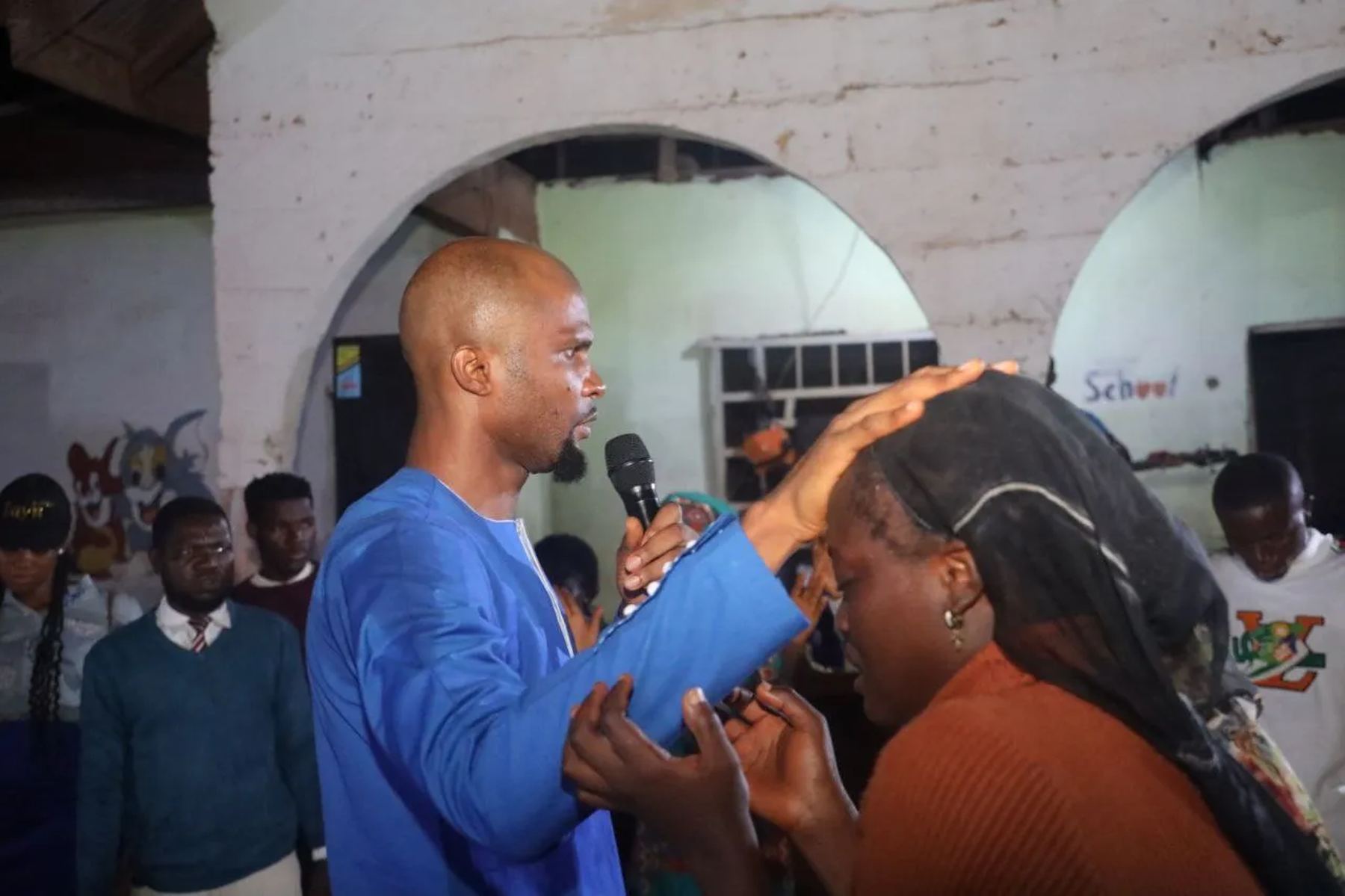 A minister with a microphone praying for a woman, his hand on her head