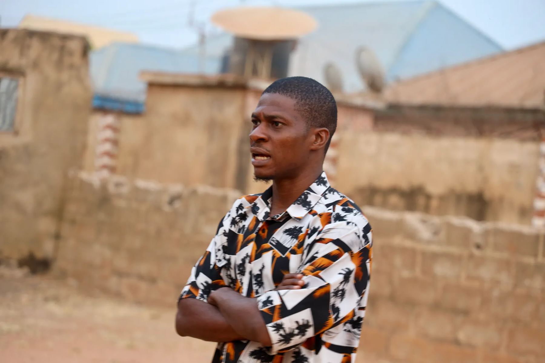 A team member standing with folded arms in a street of mud-brick walls
