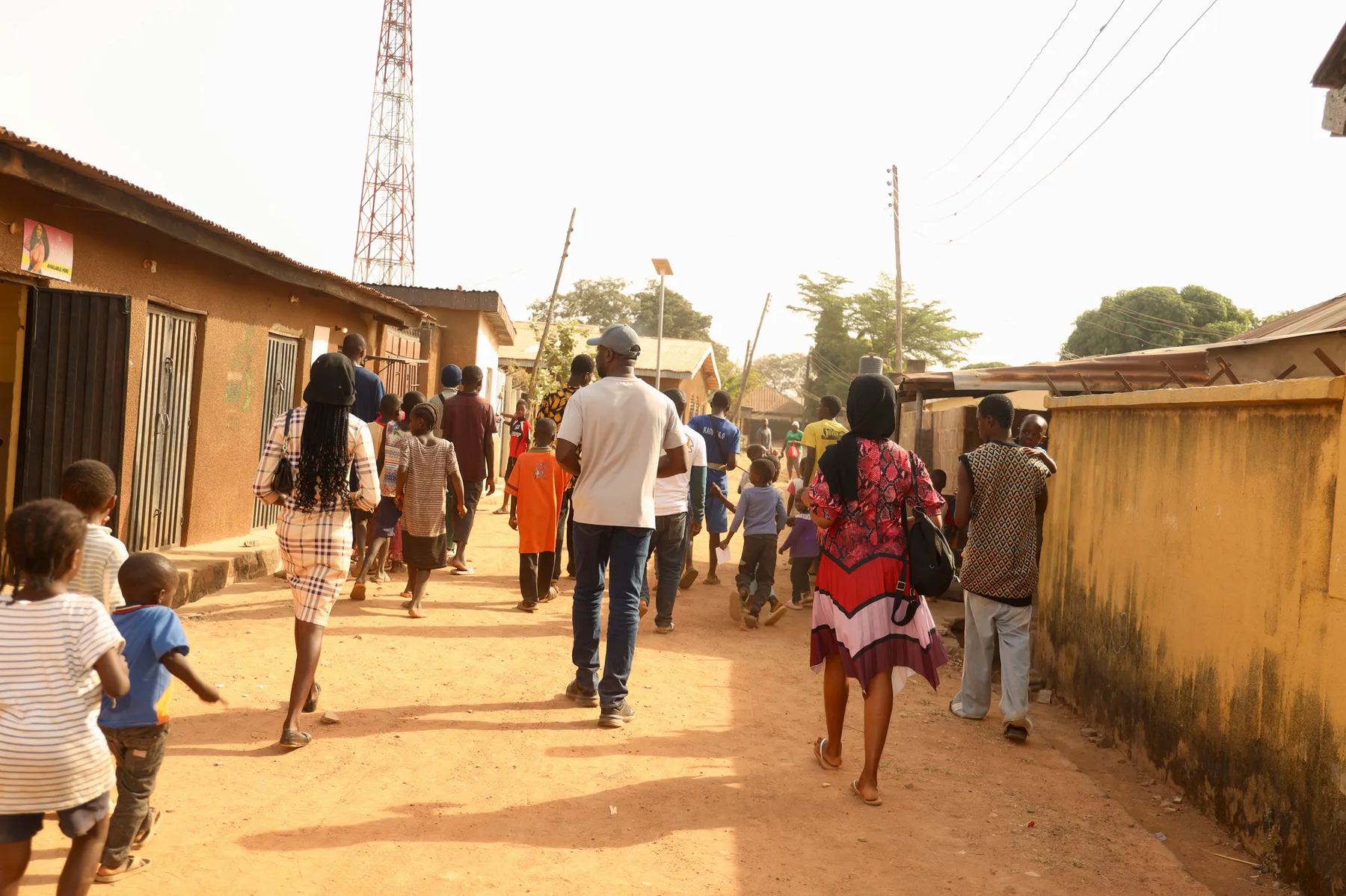 The team walking down a dusty street with children running alongside