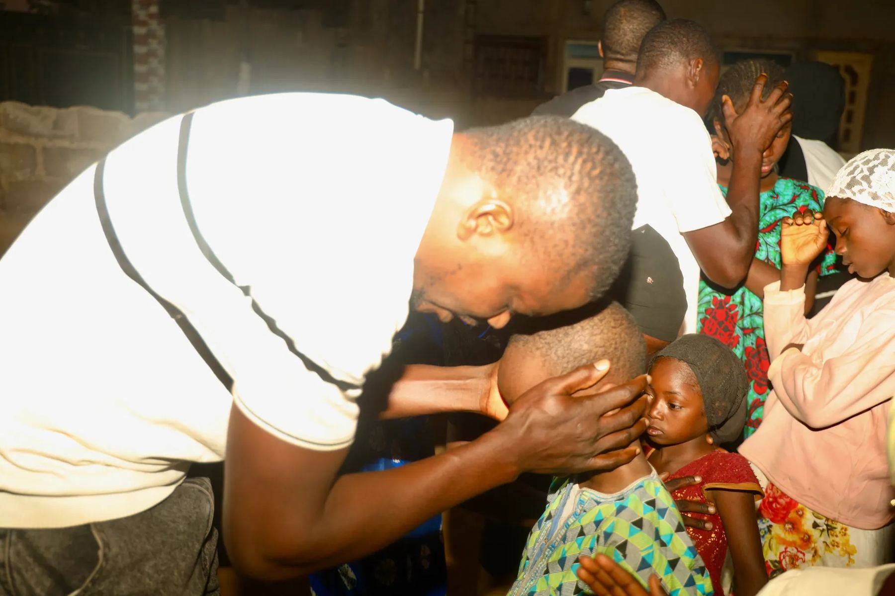 A team member bending to pray for a child, with other children nearby
