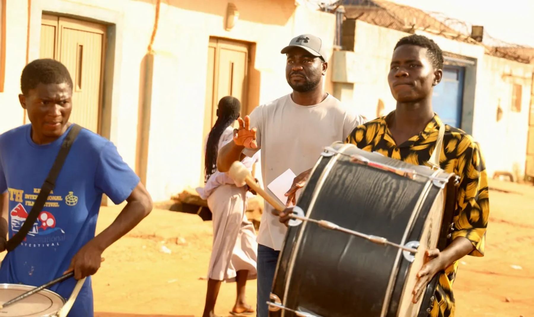 A drummer and team members walking through the street with a bass drum
