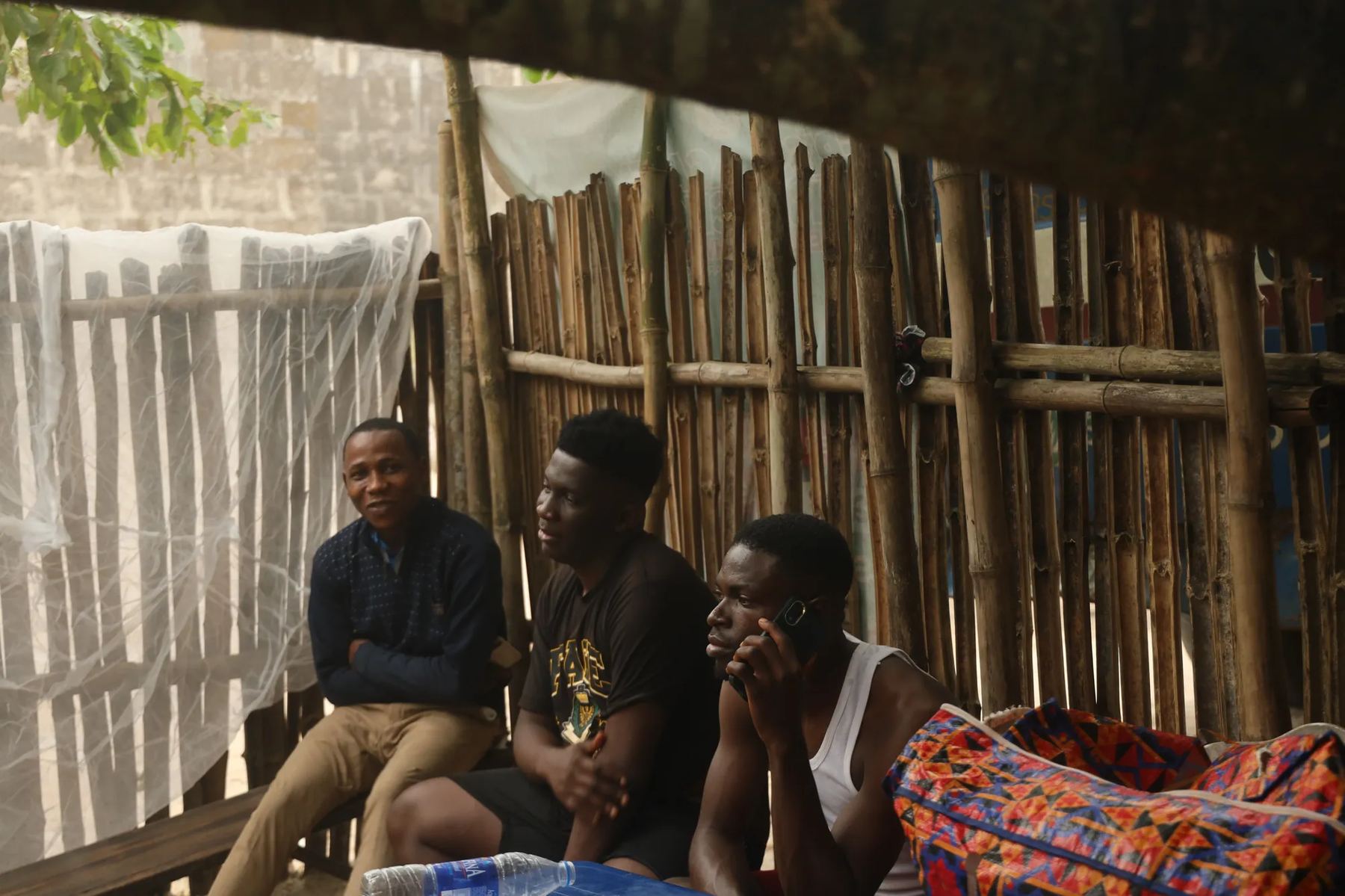 Three young men resting in a bamboo shelter