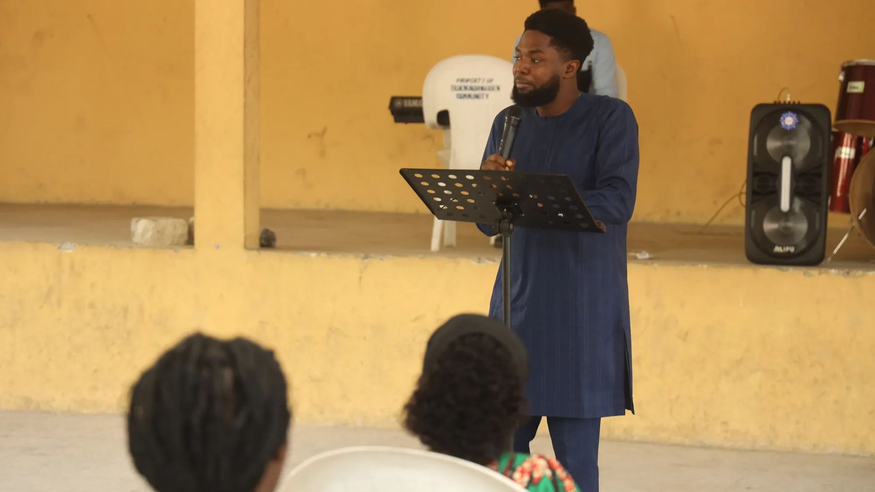 A man in a blue kaftan preaching with a microphone at a music stand
