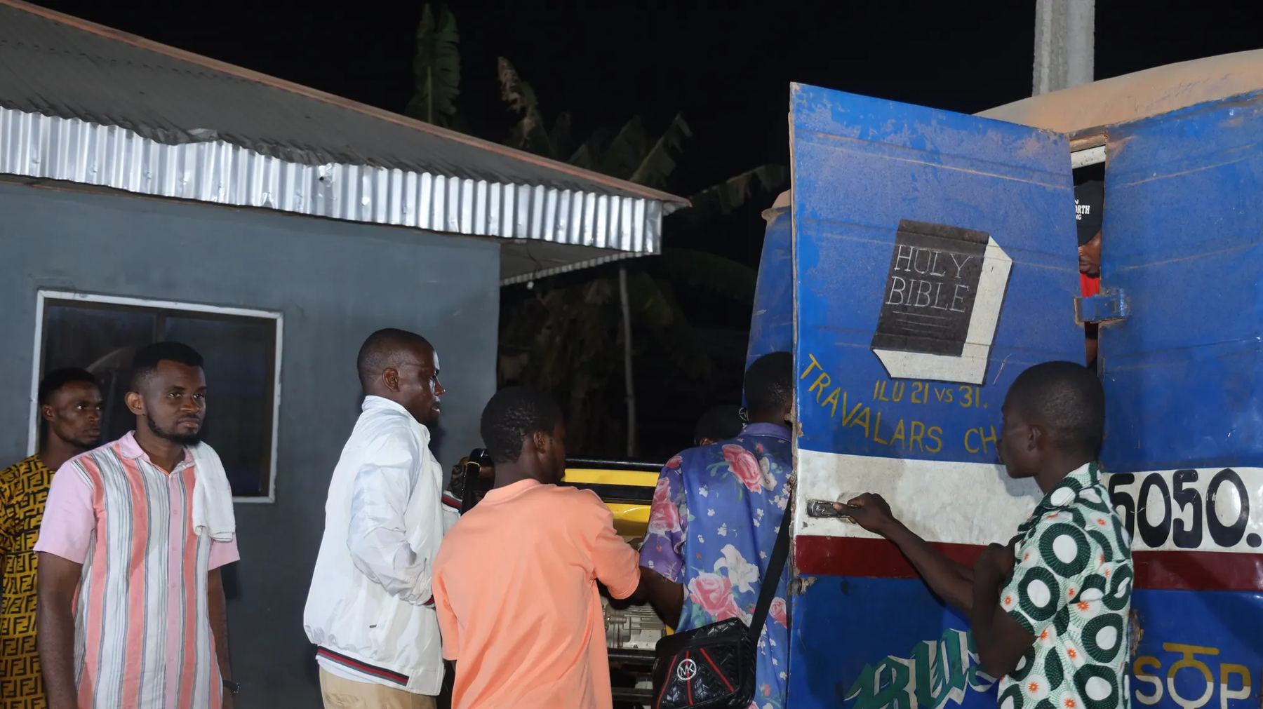 People gathered at night by a bus painted with a Holy Bible