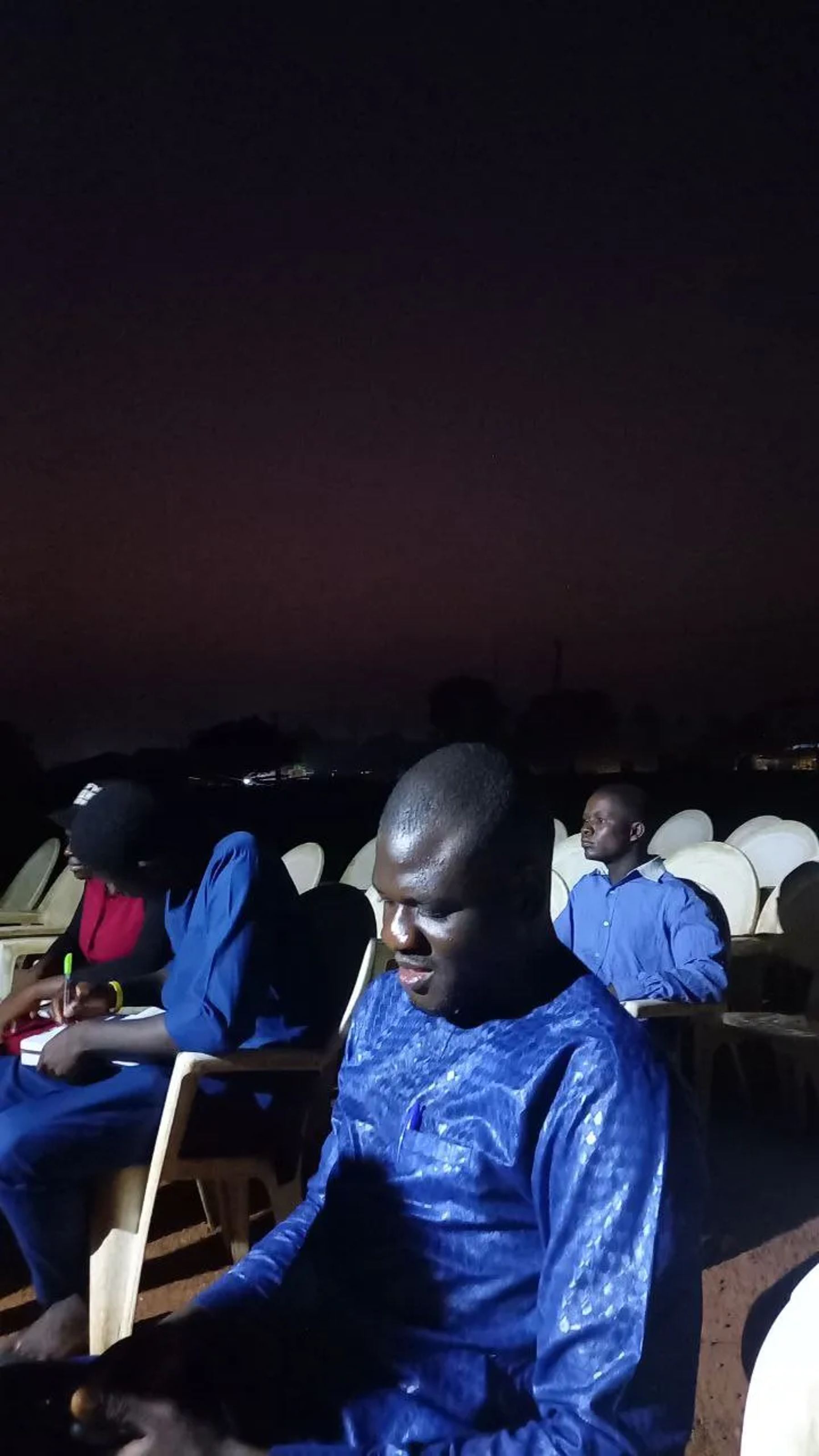A man seated at the evening meeting, reading in the dark