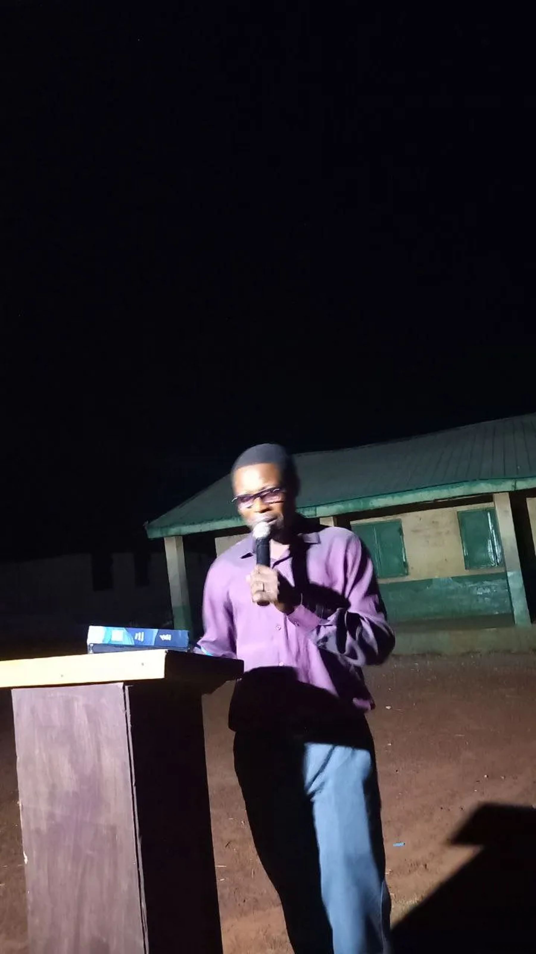 A team member preaching with a microphone at a lectern at night