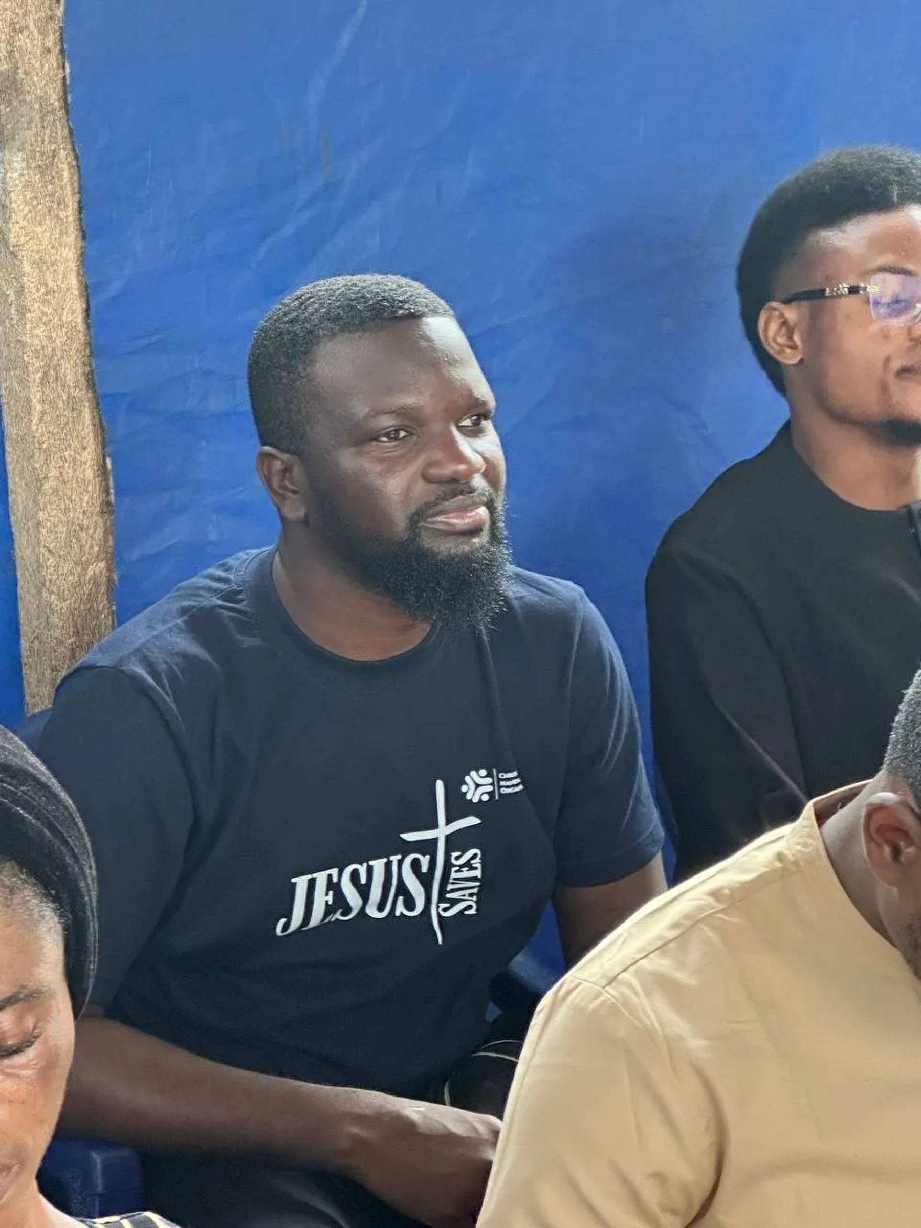 A team member in a Jesus T-shirt seated with others under the canopy
