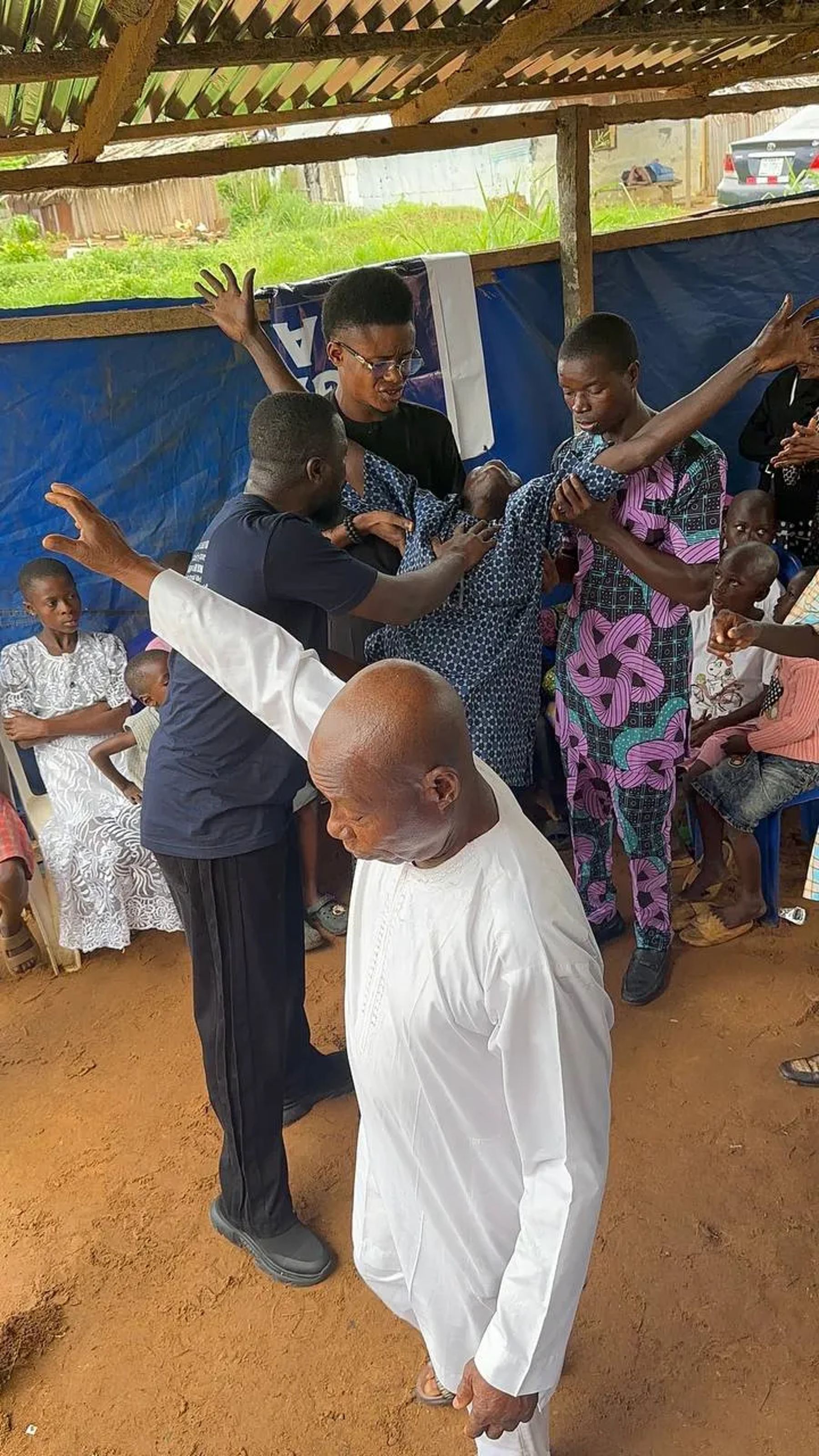 Team members and a church leader praying with raised hands over people under the canopy
