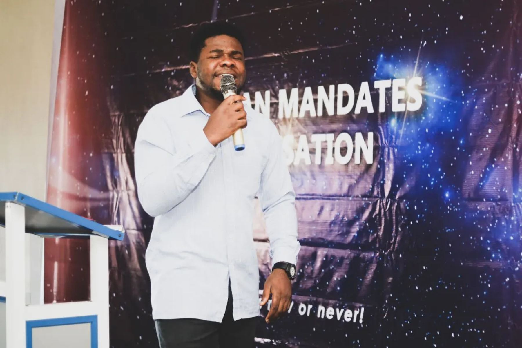 A man singing with a microphone in front of the CMO banner