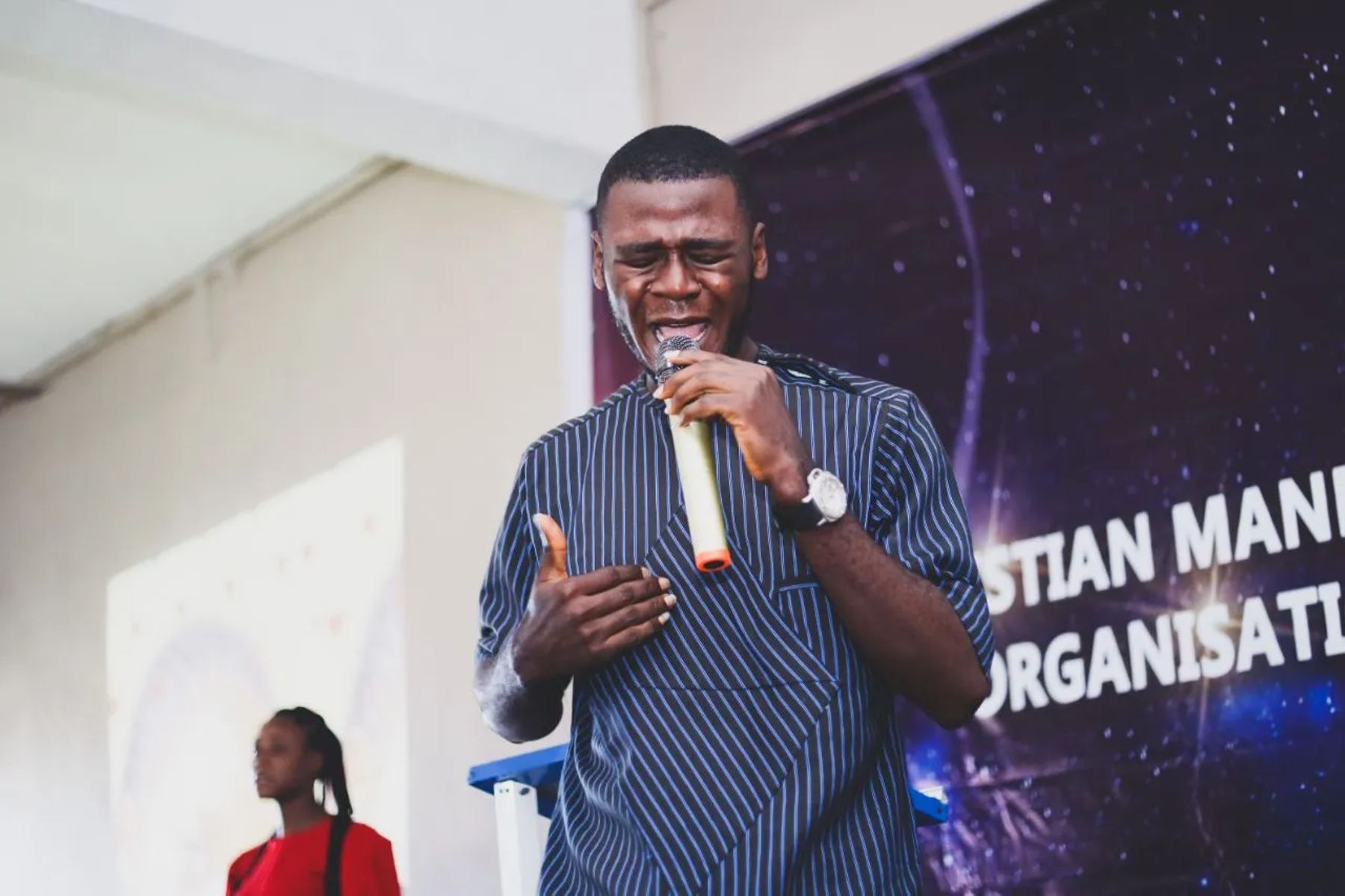A man praying with a microphone in front of the banner
