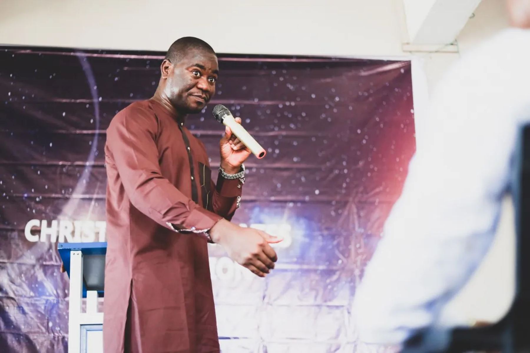 A minister in a maroon kaftan speaking with a microphone