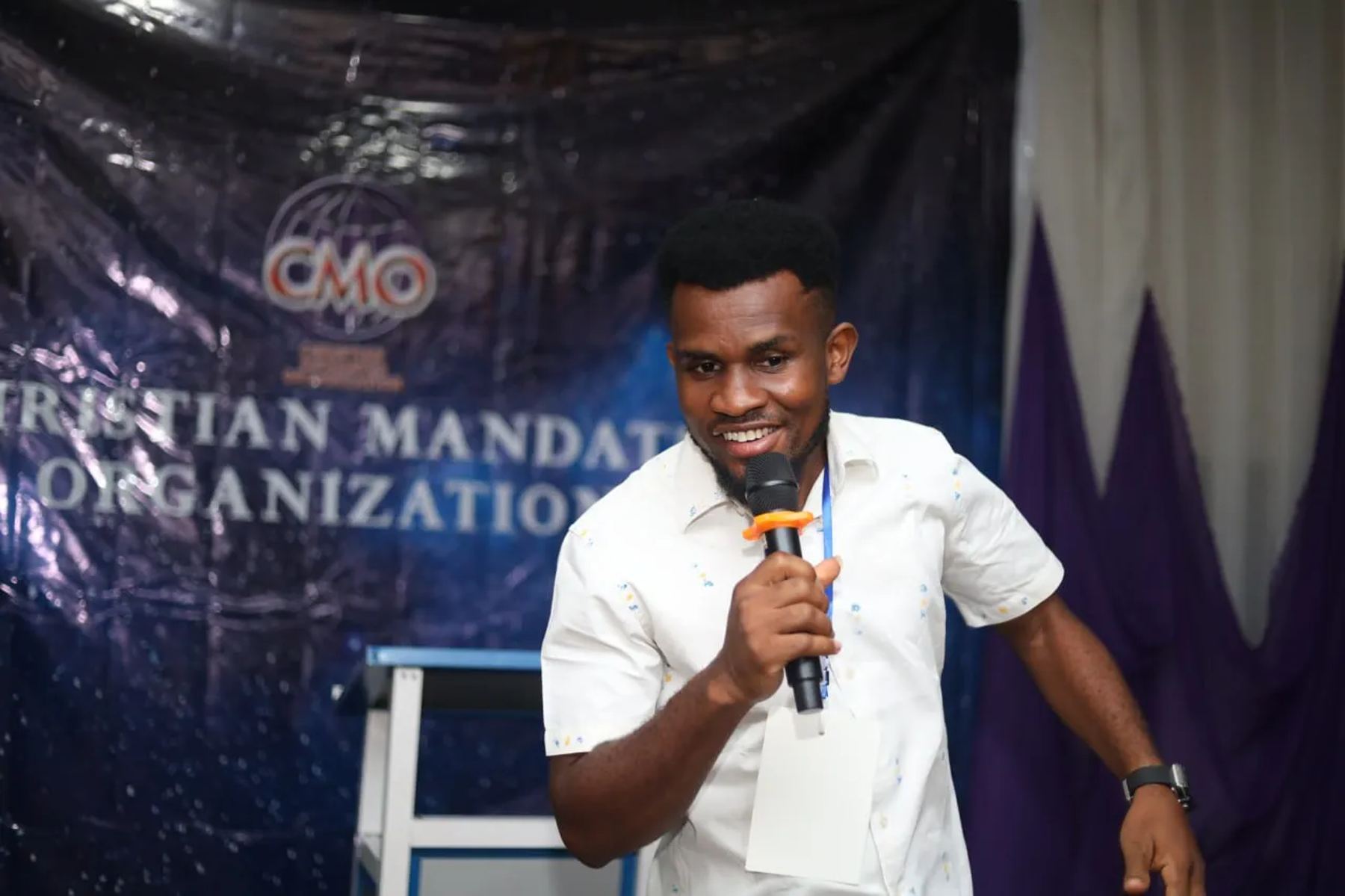 A speaker with a microphone smiling in front of the CMO banner