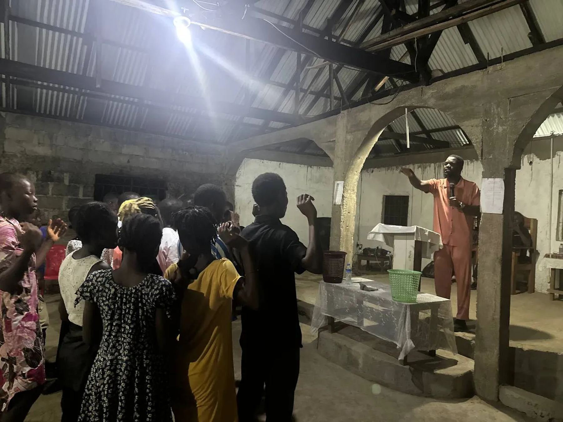 A man in orange praying with a raised hand over people at the front of the church