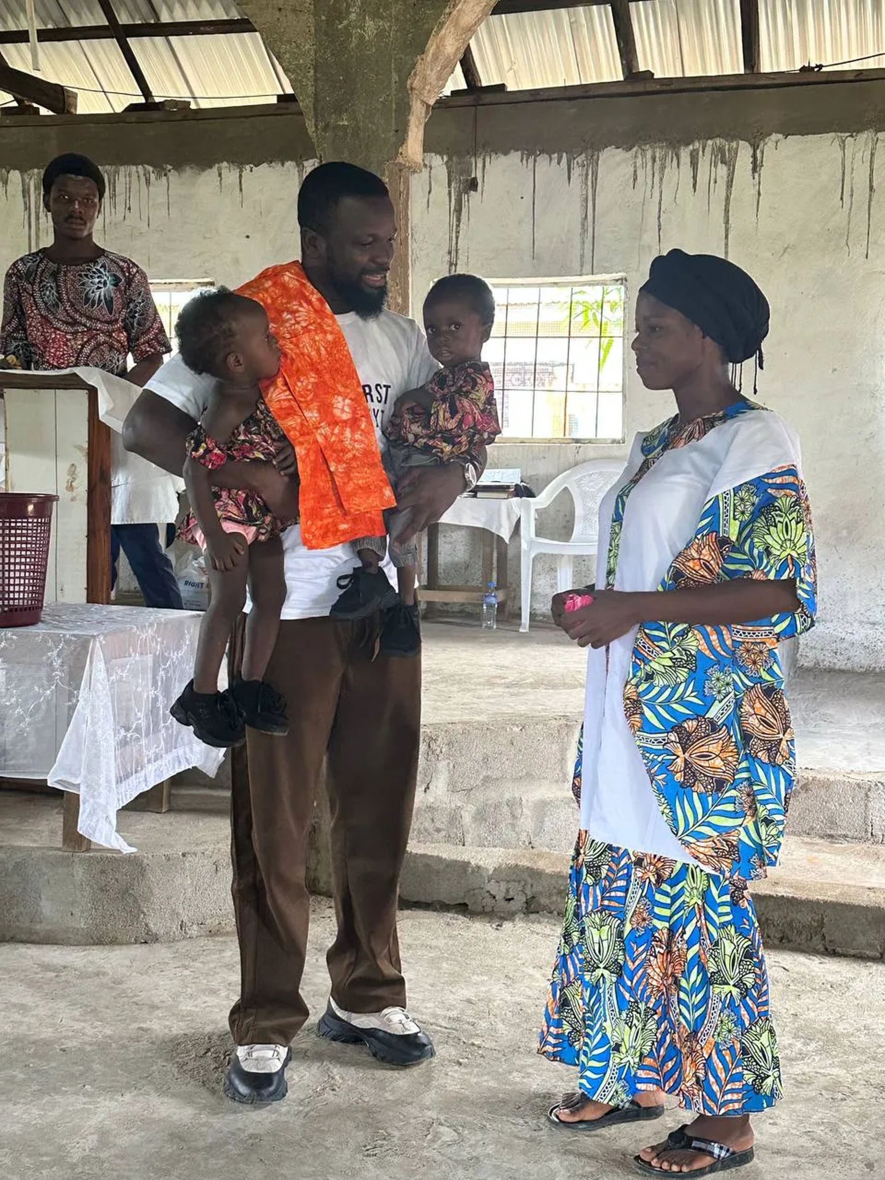 A team member holding two young children beside a woman in a patterned dress