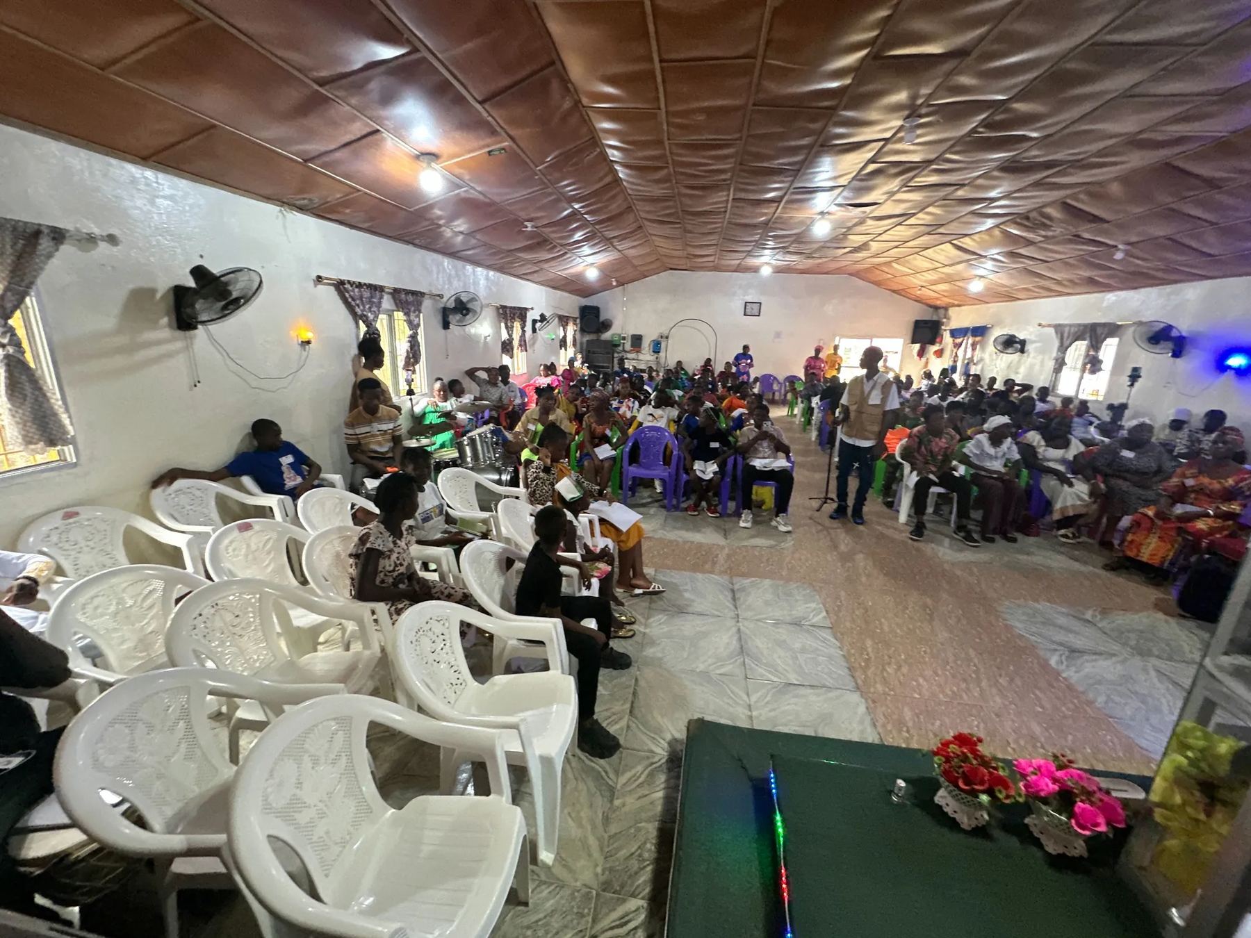 A long view of the church hall filling with people on plastic chairs
