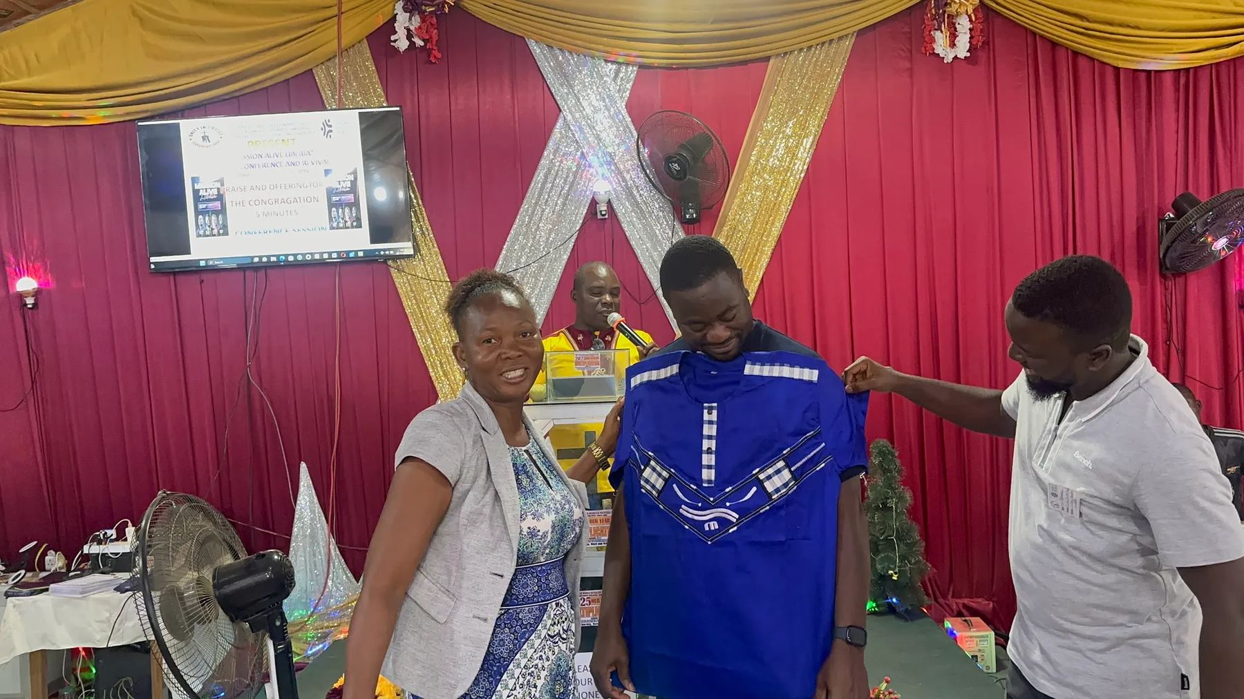 A team member being presented with a blue embroidered shirt at the front of the church