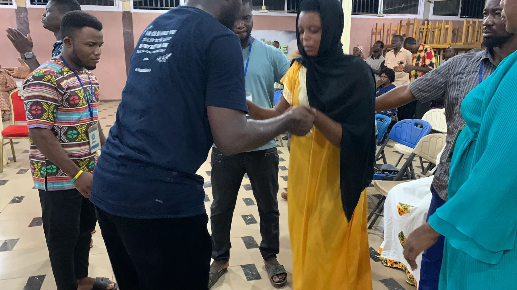 A team member praying with a woman in a black head covering and yellow dress