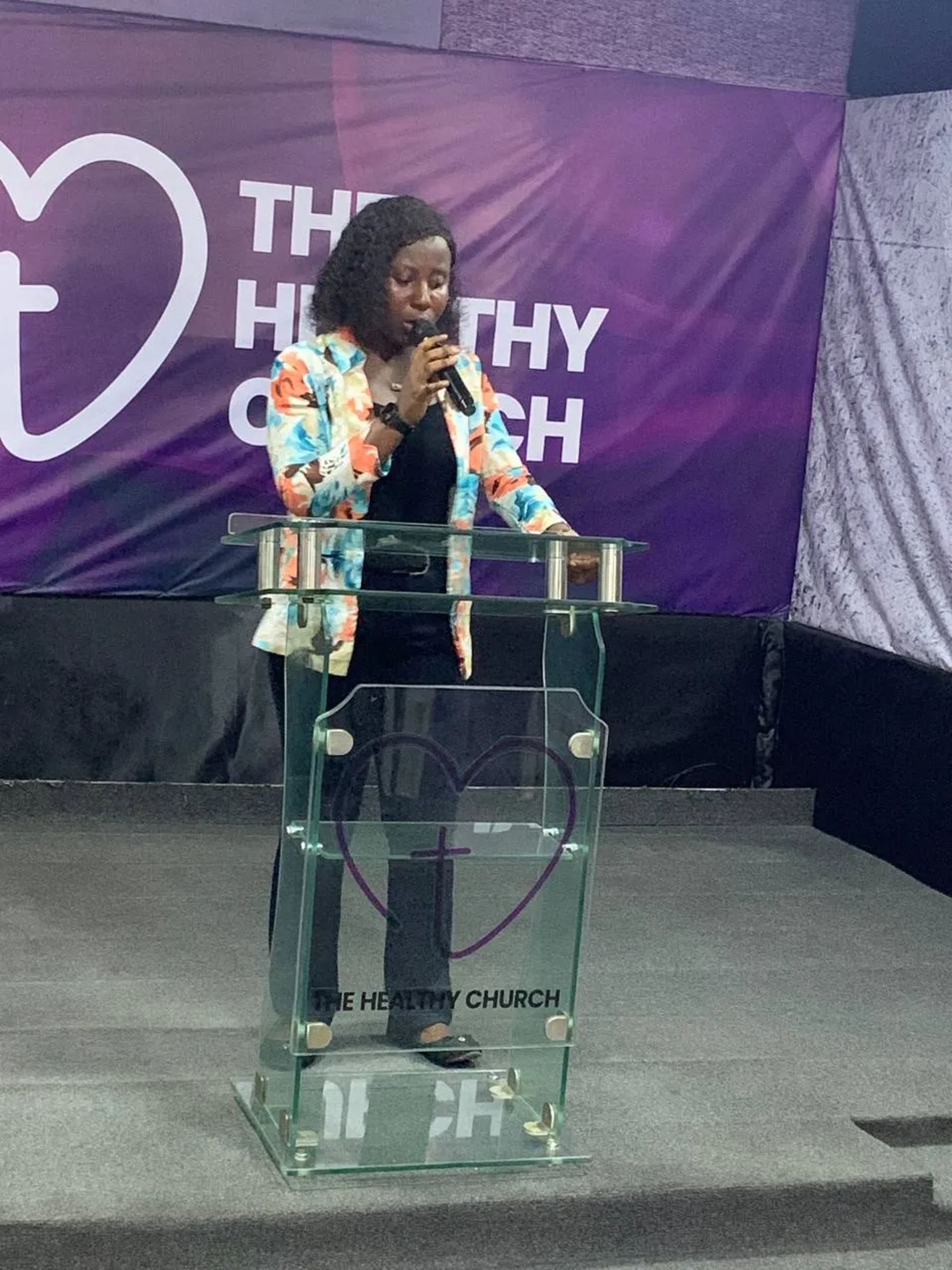 A woman speaking at a glass lectern at The Healthy Church
