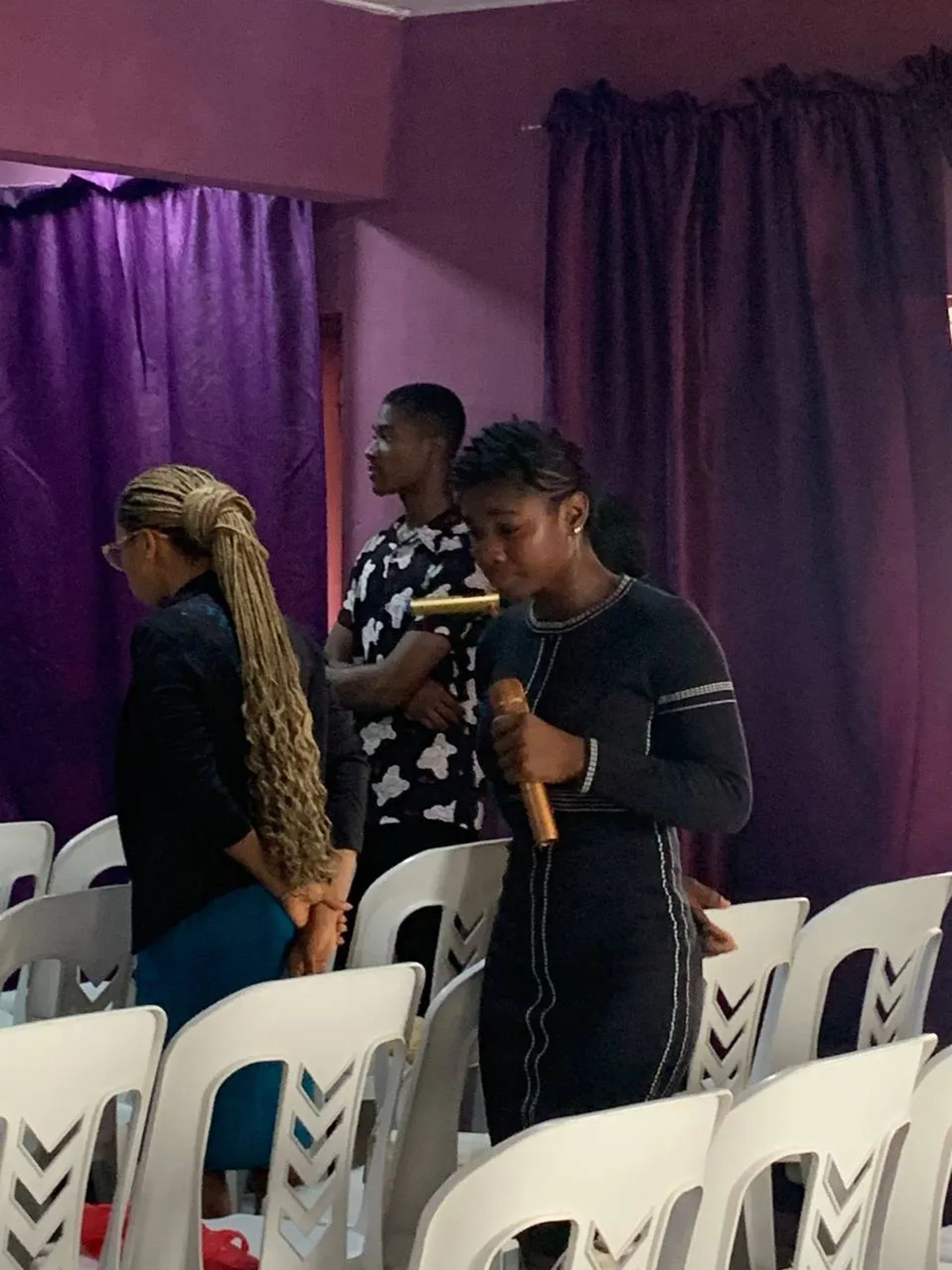A woman leading prayer with a microphone among the chairs