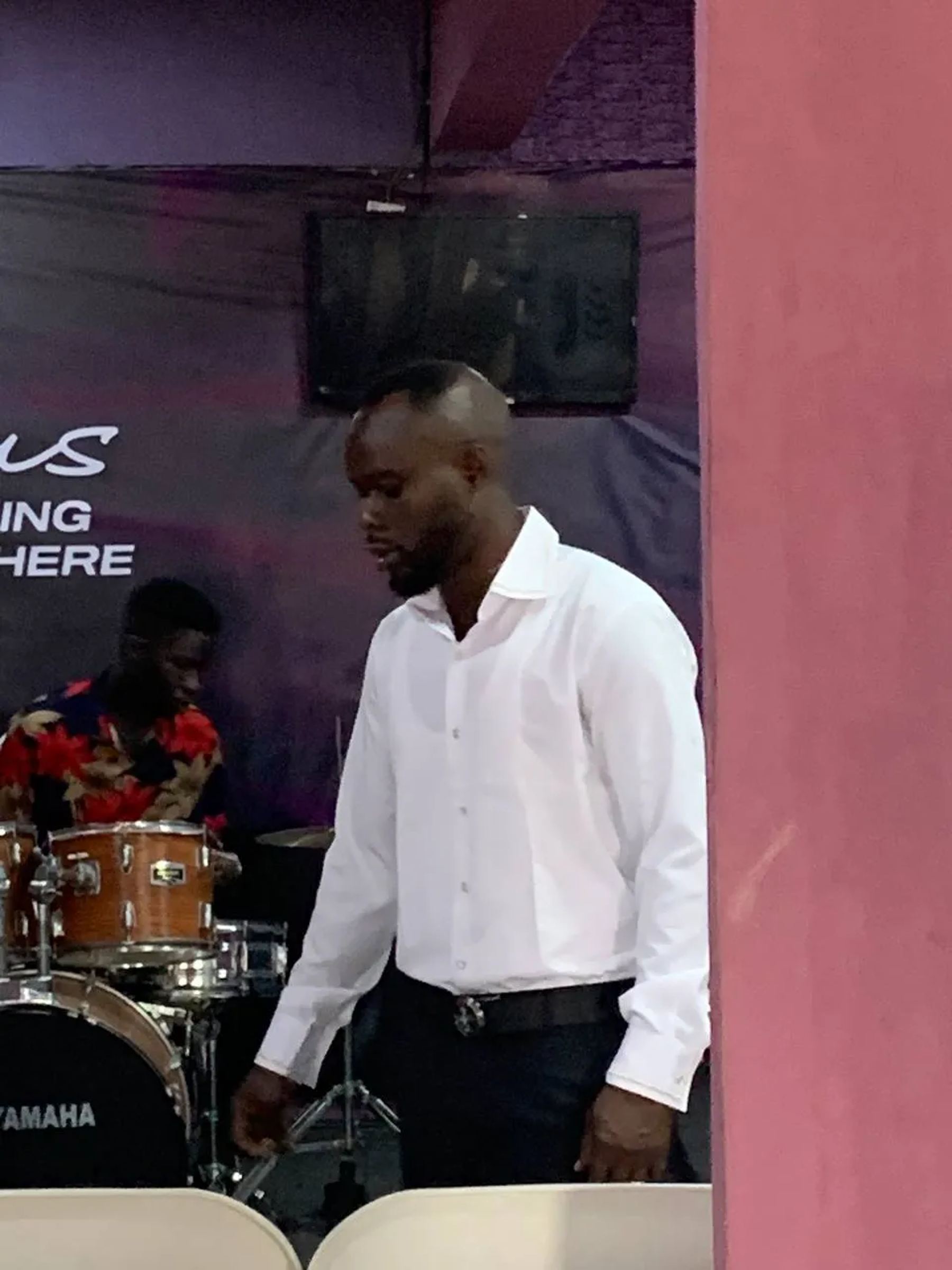 A man in a white shirt standing near the drums at the front of the church