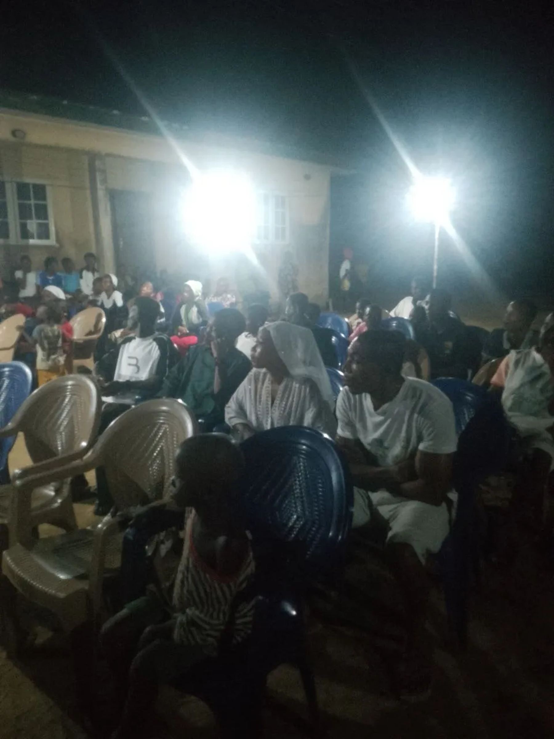 The crowd seated under floodlights in front of a building