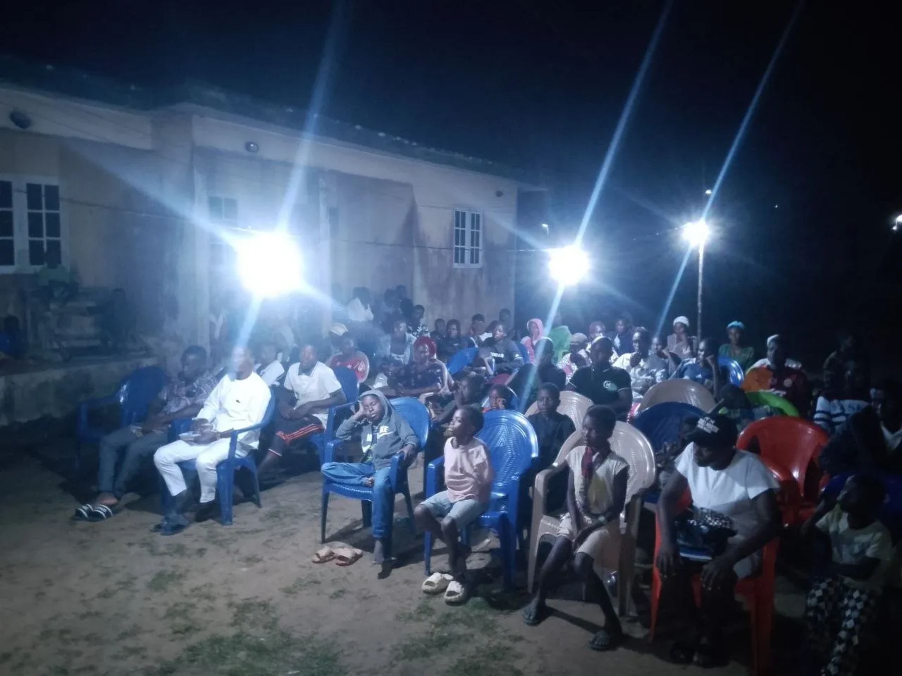 A large crowd seated on blue and red chairs under floodlights at night