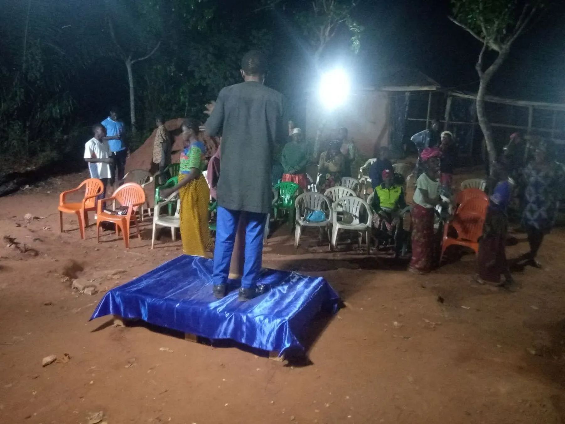 A preacher on a blue platform before the crowd at night