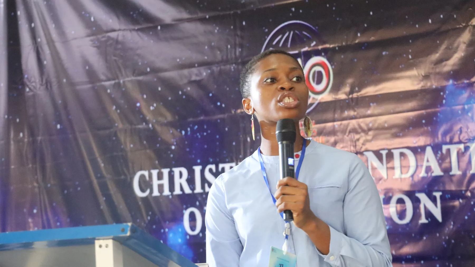 A woman speaking into a microphone at the lectern in front of the CMO banner