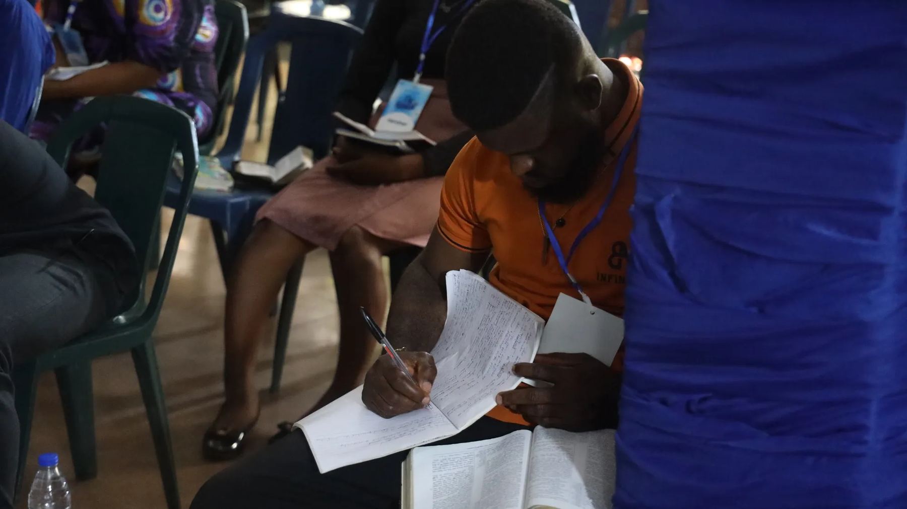 A participant writing notes with his Bible open on his lap