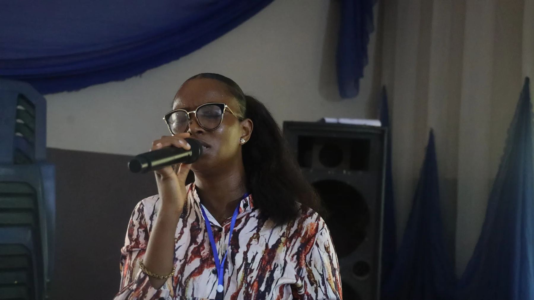 A woman in glasses speaking into a microphone in the hall