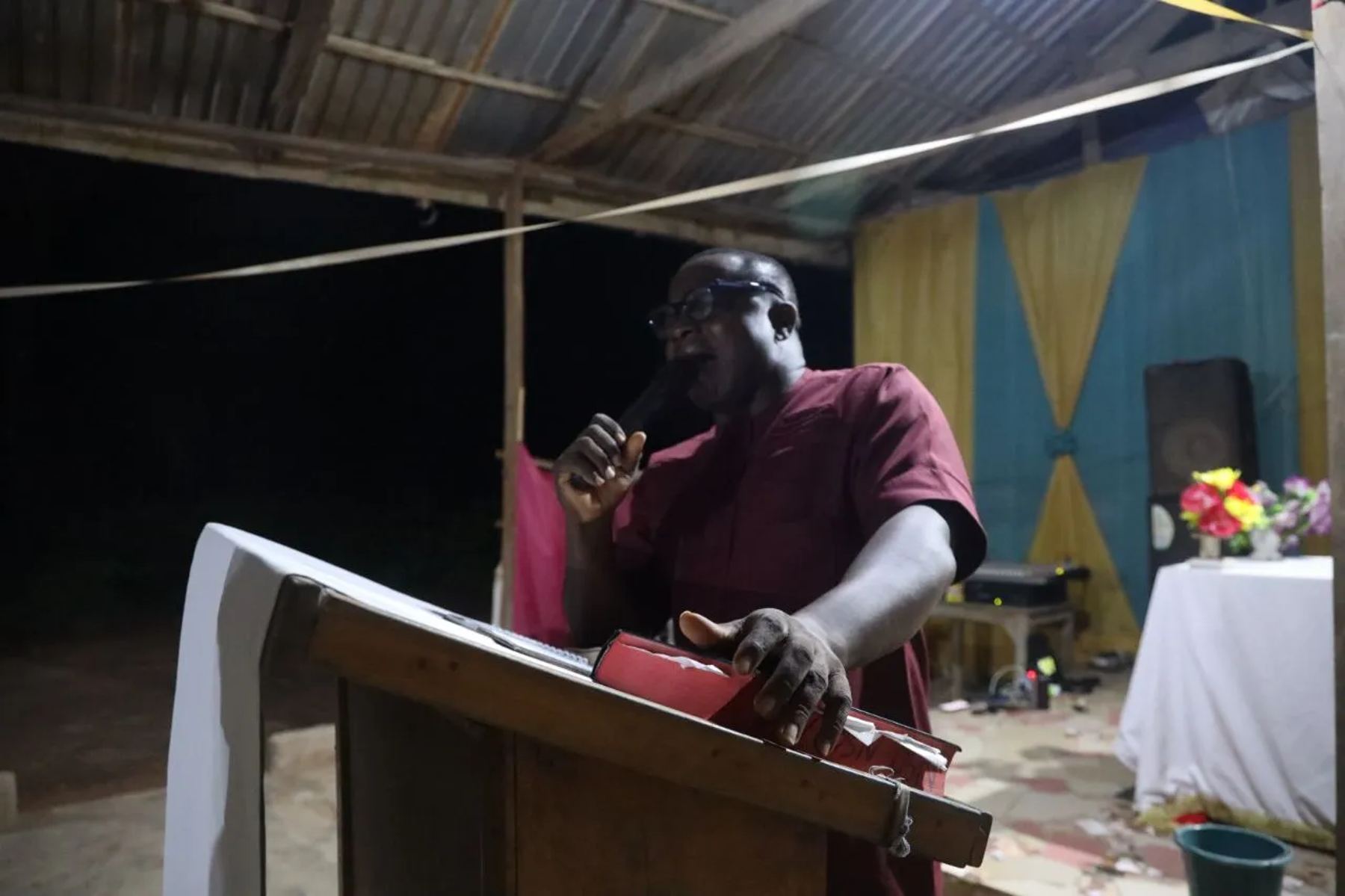 A preacher at a wooden lectern under the church shelter at night